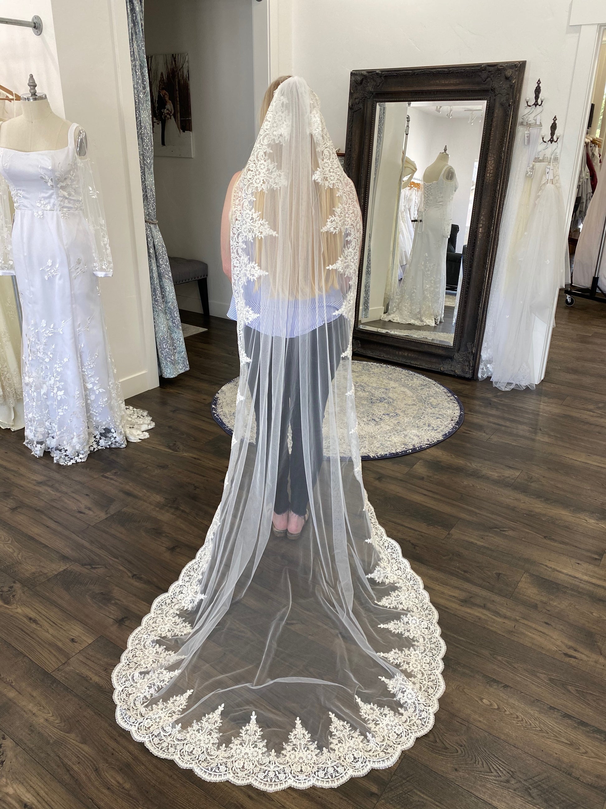 April veil in chapel length spread out behind the bride in a fan, emphasizing the dramatic length and delicate lace edging.