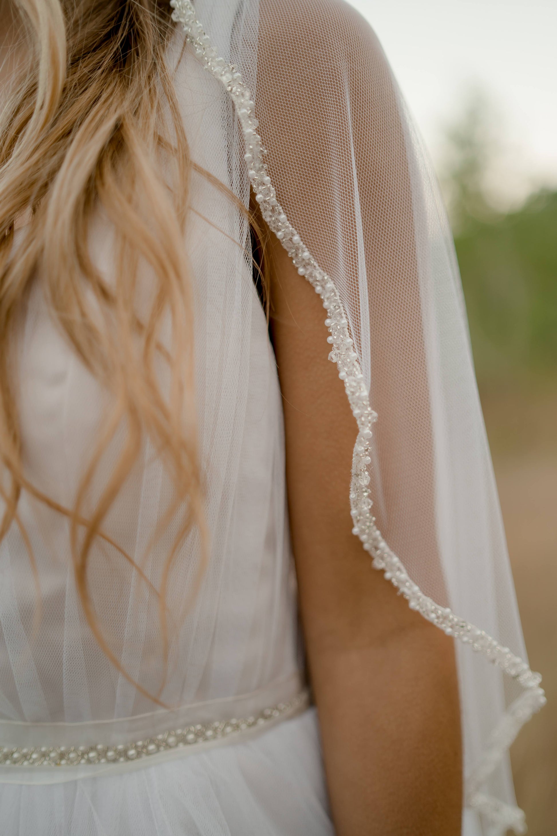 A close up shot of a bride wearing the Lena veil with beaded lace trim, Persephone gown, and Fleur belt.