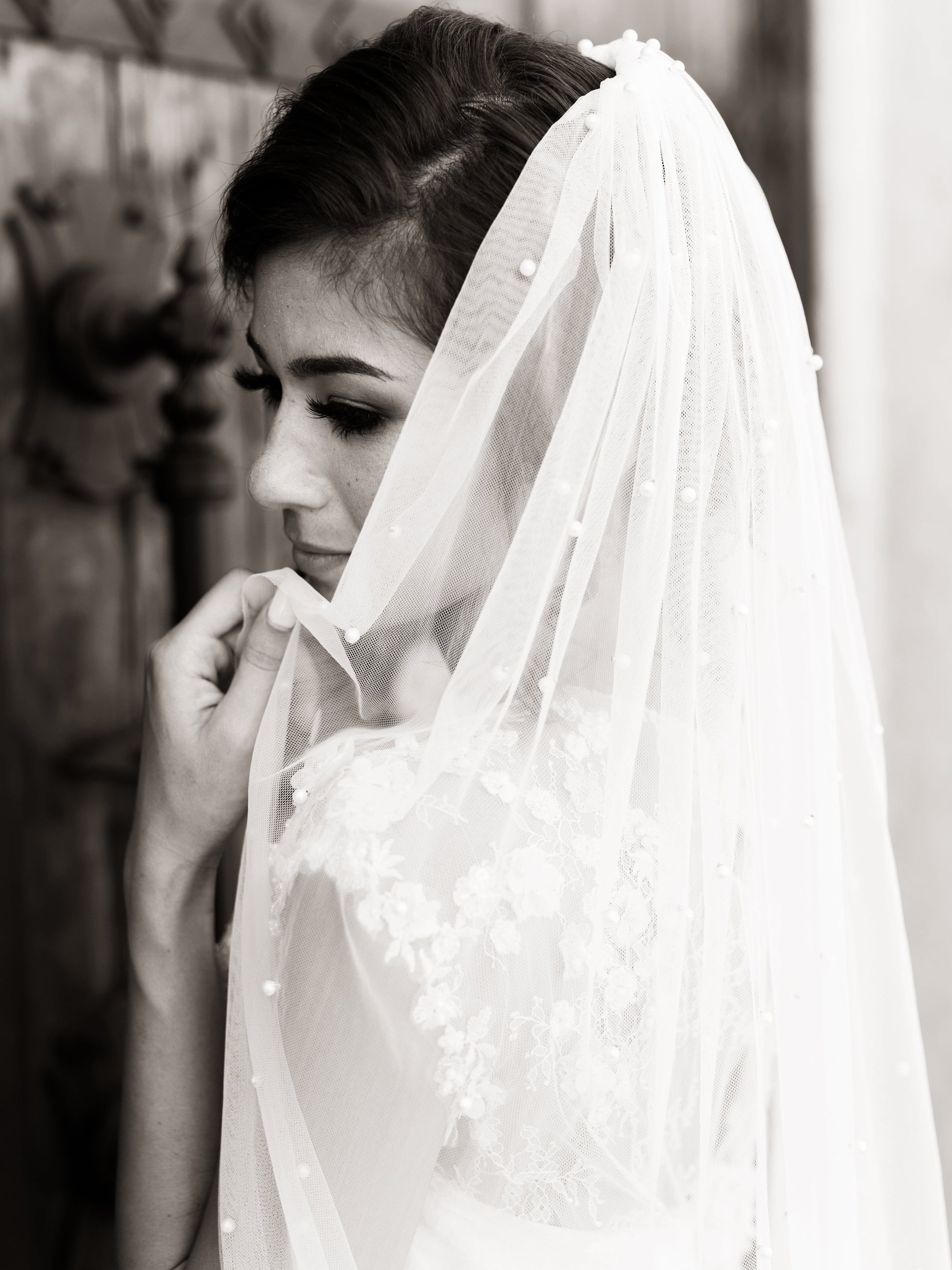 An upclose image of a brides shoulders up;  she is wearing the Leah pearl beaded veil and the Naomi gown. The Veil is pulled to the side showing off the pearls and the spacing.