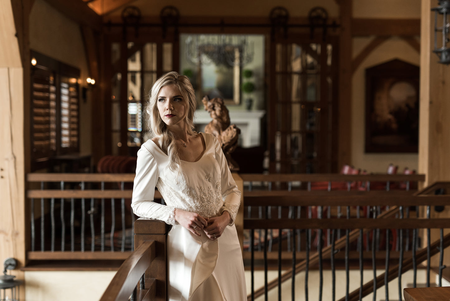 Bride leaned slightly on a railing, highlighting curved front neckline, bodice lace, and long sleeves with lace.