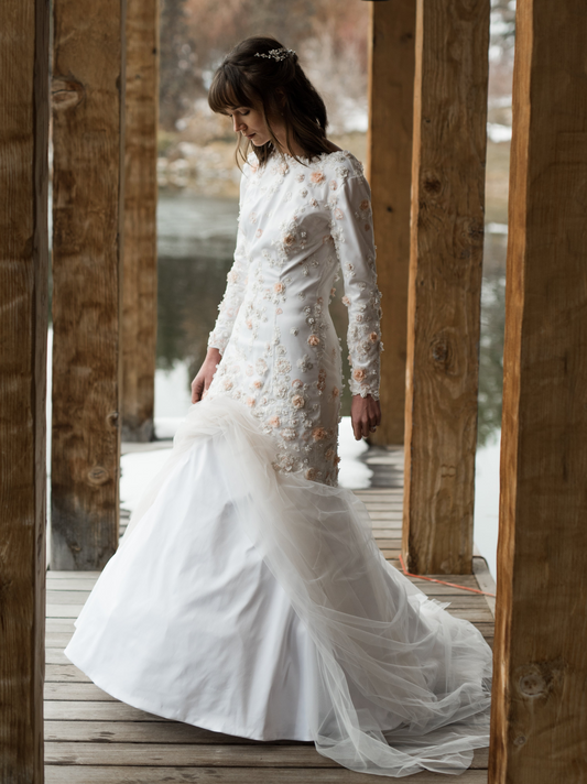 The Lydia gown shown here on a bride standing on a dock, shows the Fitted satin silhouette with floral lace overlay at mermaid seam  . The gown is shown in satin not crepe, the crepe would be just as fitted but more matte.