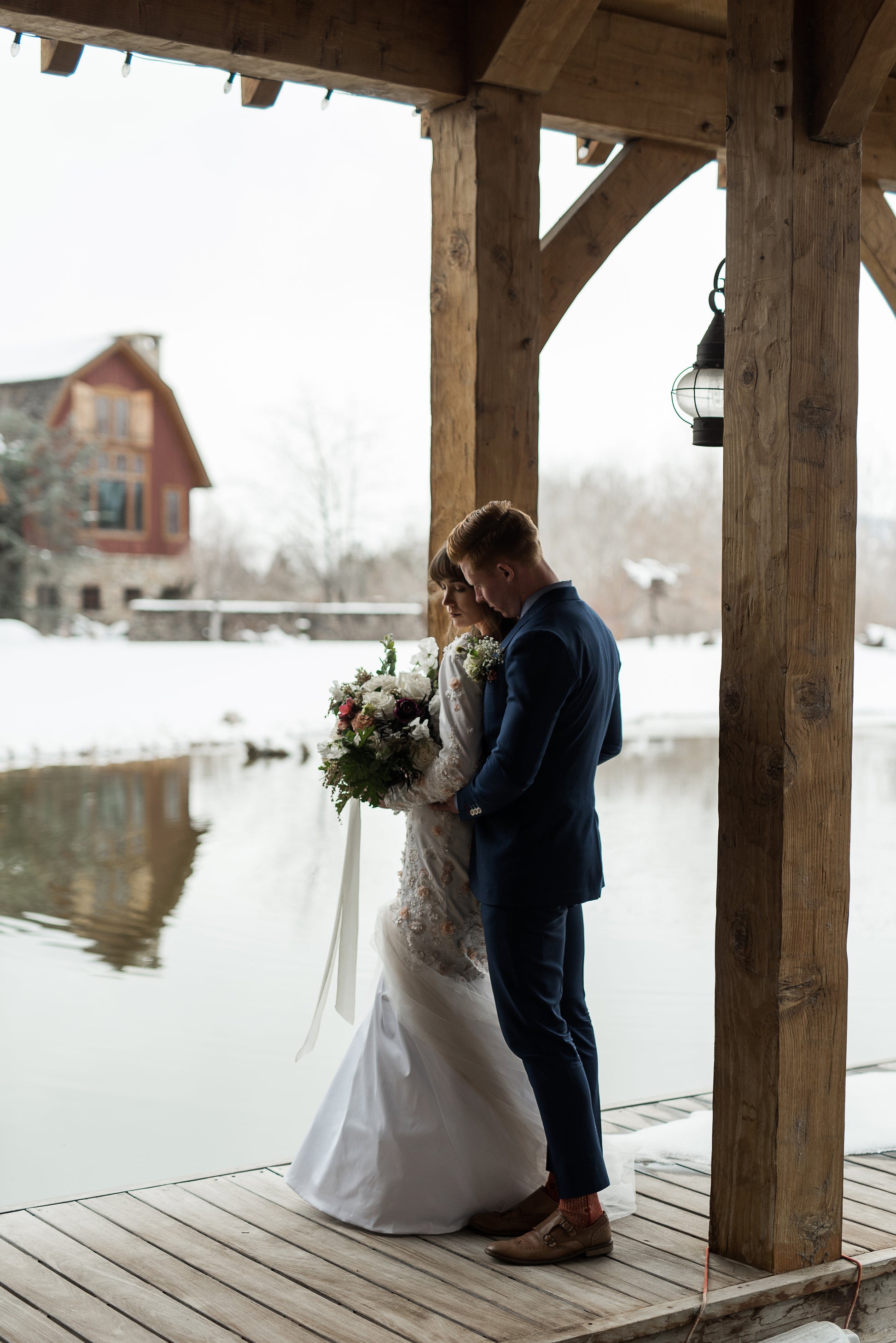 The lydia gown is shown here on a bride being hugged from behind by her groom. You can see the Mermaid silhouette gown with scoop back and tullé train that is swept to the side.