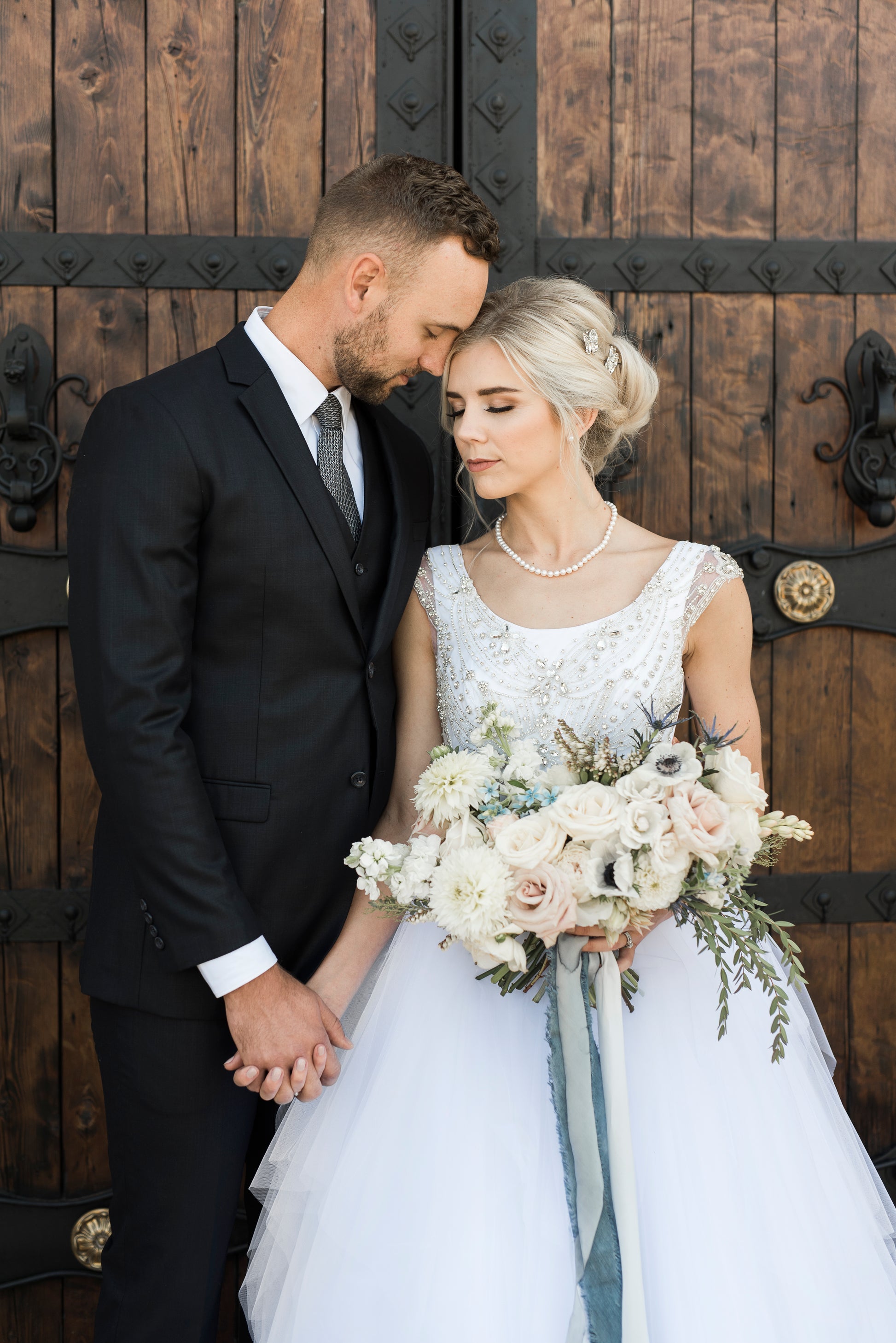 Bride and groom stand together in front of castle doors; you can see the Front view of the Georgia wedding dress with scoop neckline, rhinestone bodice, and tiered tulle skirt.
