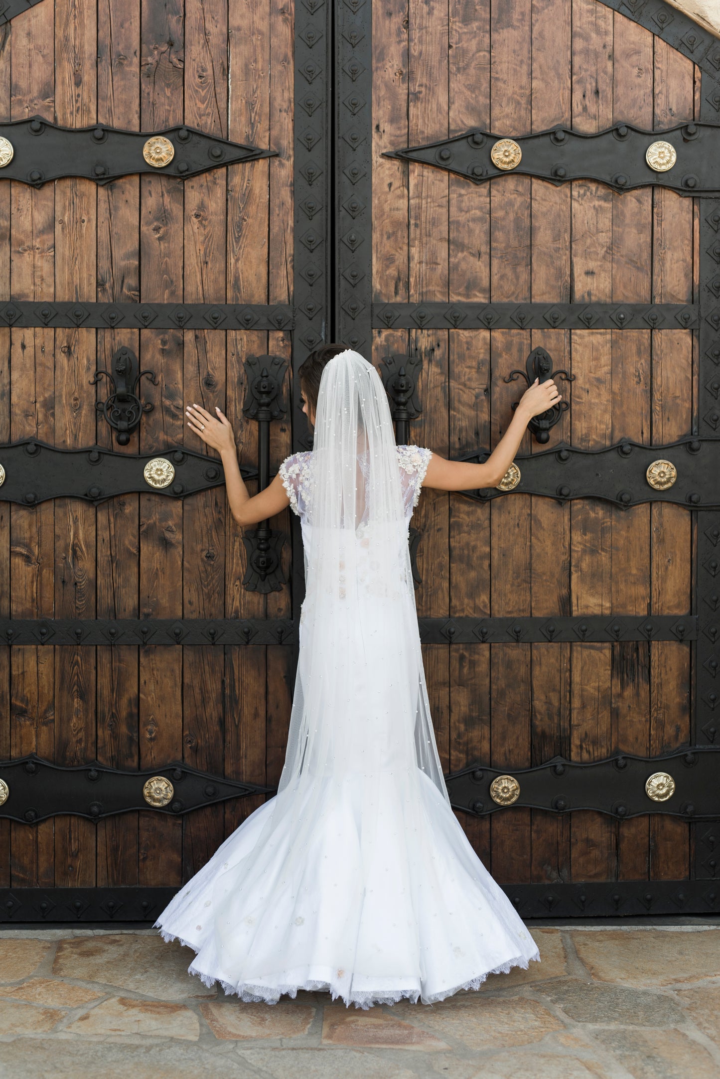 A full back view of the naomi mermaid wedding gown paired with the leah veil in puddle length for an embelished romantic look