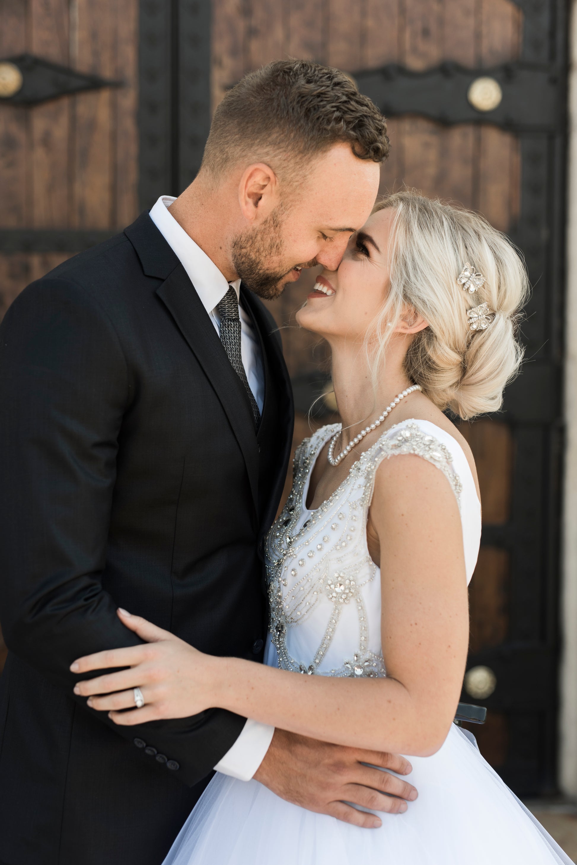 Bride leaning in to kiss her groom showing the Side view of the georgia gown, highlighting bodice fit, beading and sleeves.