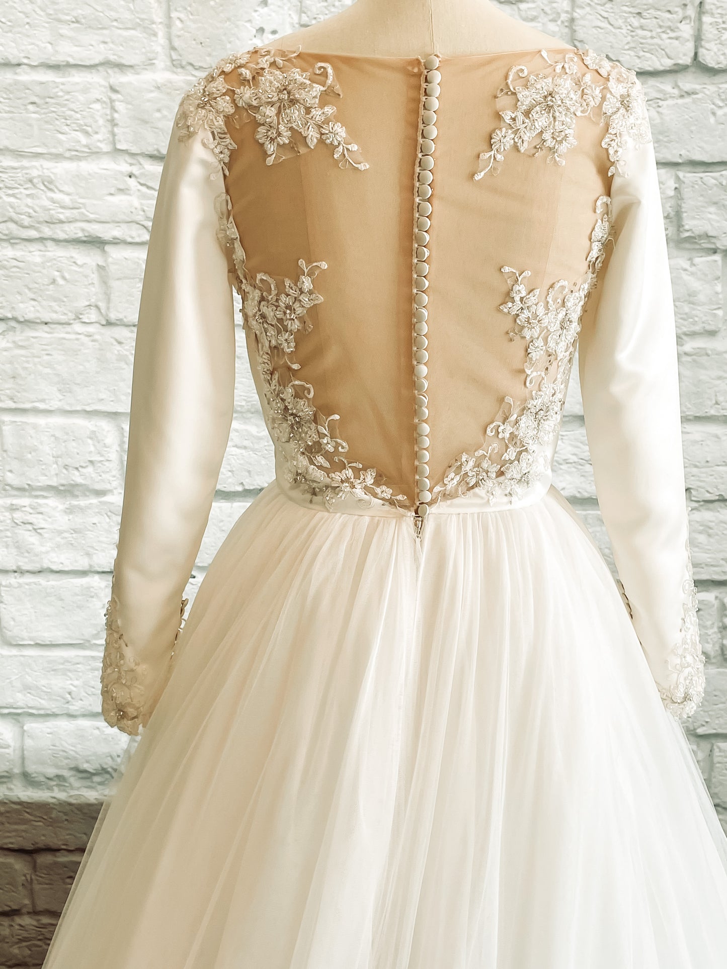 Back view of the Ava wedding dress showing illusion tulle framed by floral lace appliqué and satin-covered buttons down the spine.