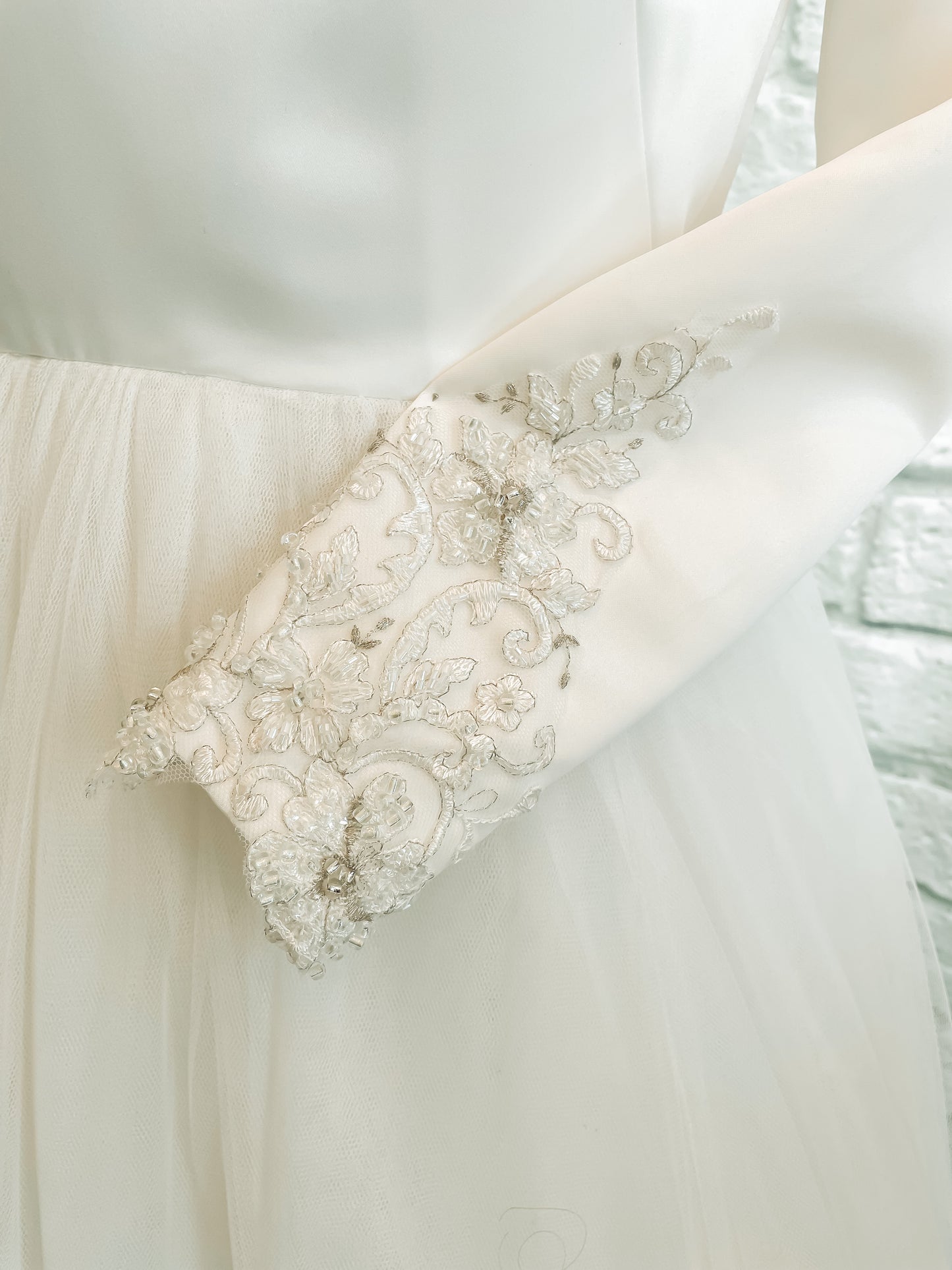Detail shot of Ava gown's long satin sleeve ending in a delicate lace.