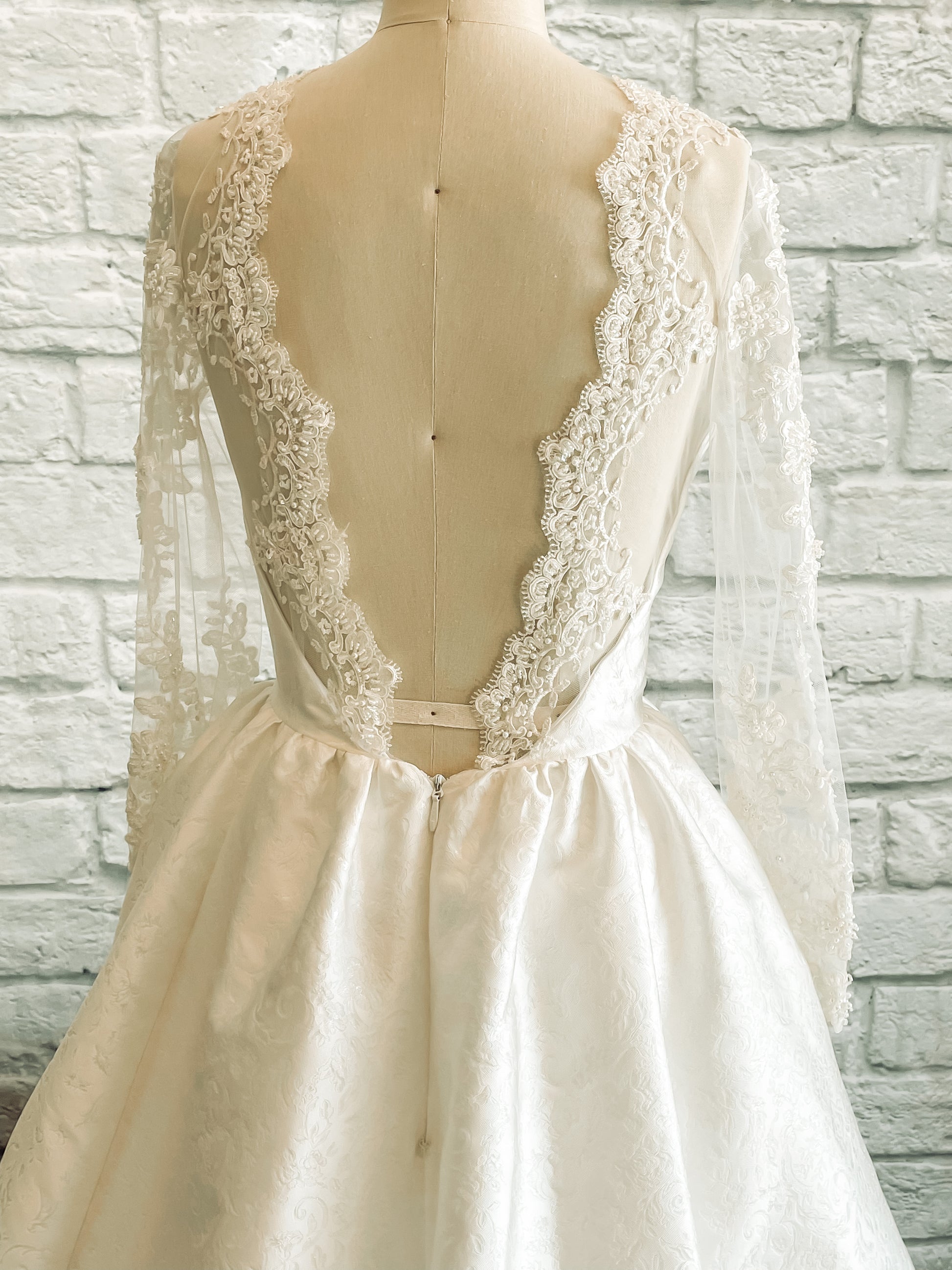 close up view of the Back of the Gemma gown highlighting illusion scooped back with beaded lace scallop and gathered full skirt.