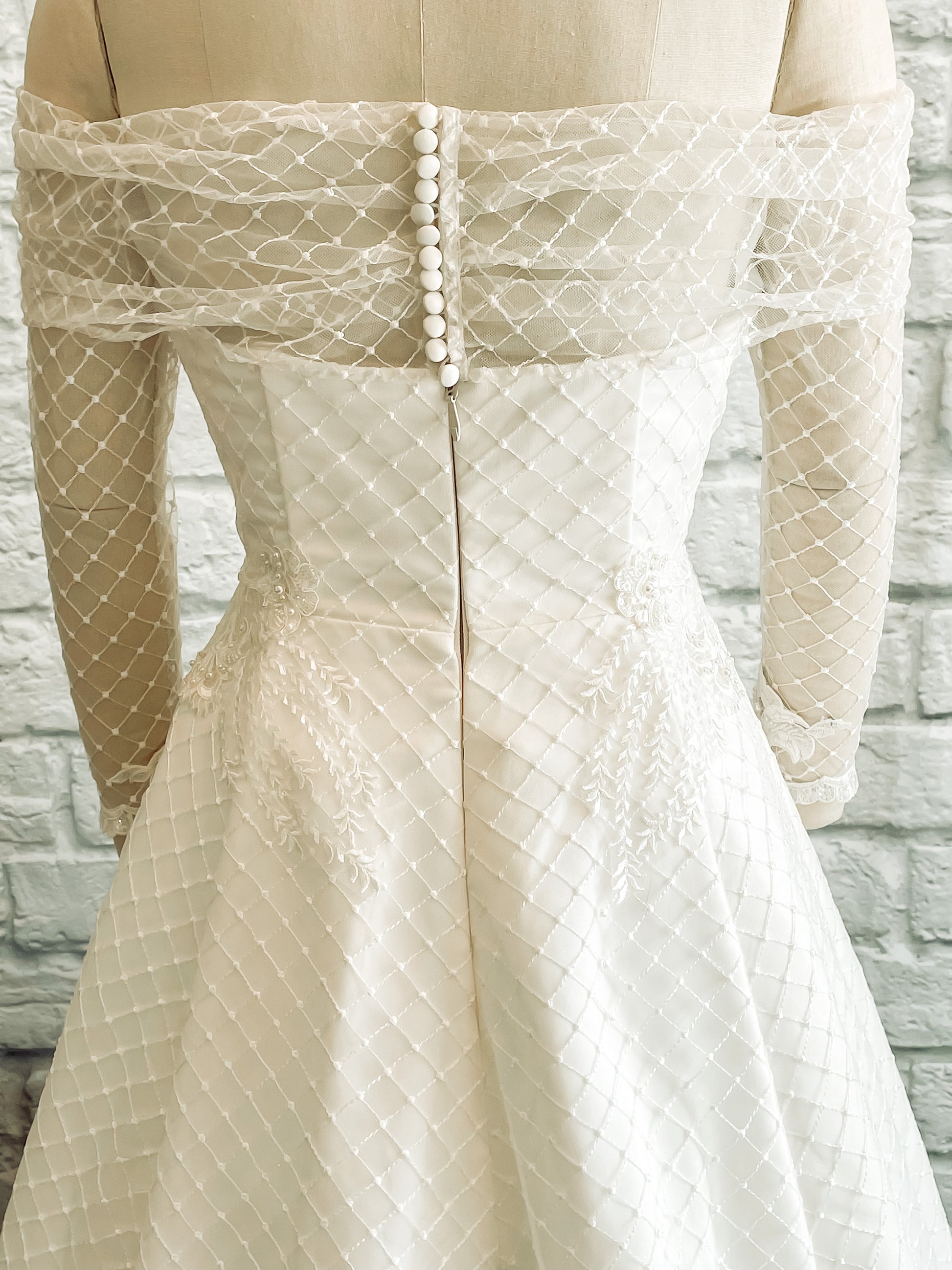 An up close shot of the back bodice of the Virginia gown; featuring the hidden bridal zipper, diamond tulle, hand placed lace and bridal buttons.
