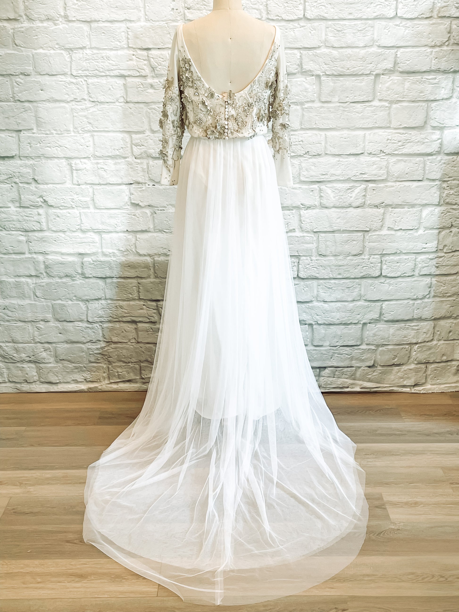 Back view of the gown showing scoop-back bodice, satin-covered buttons, and soft train.
