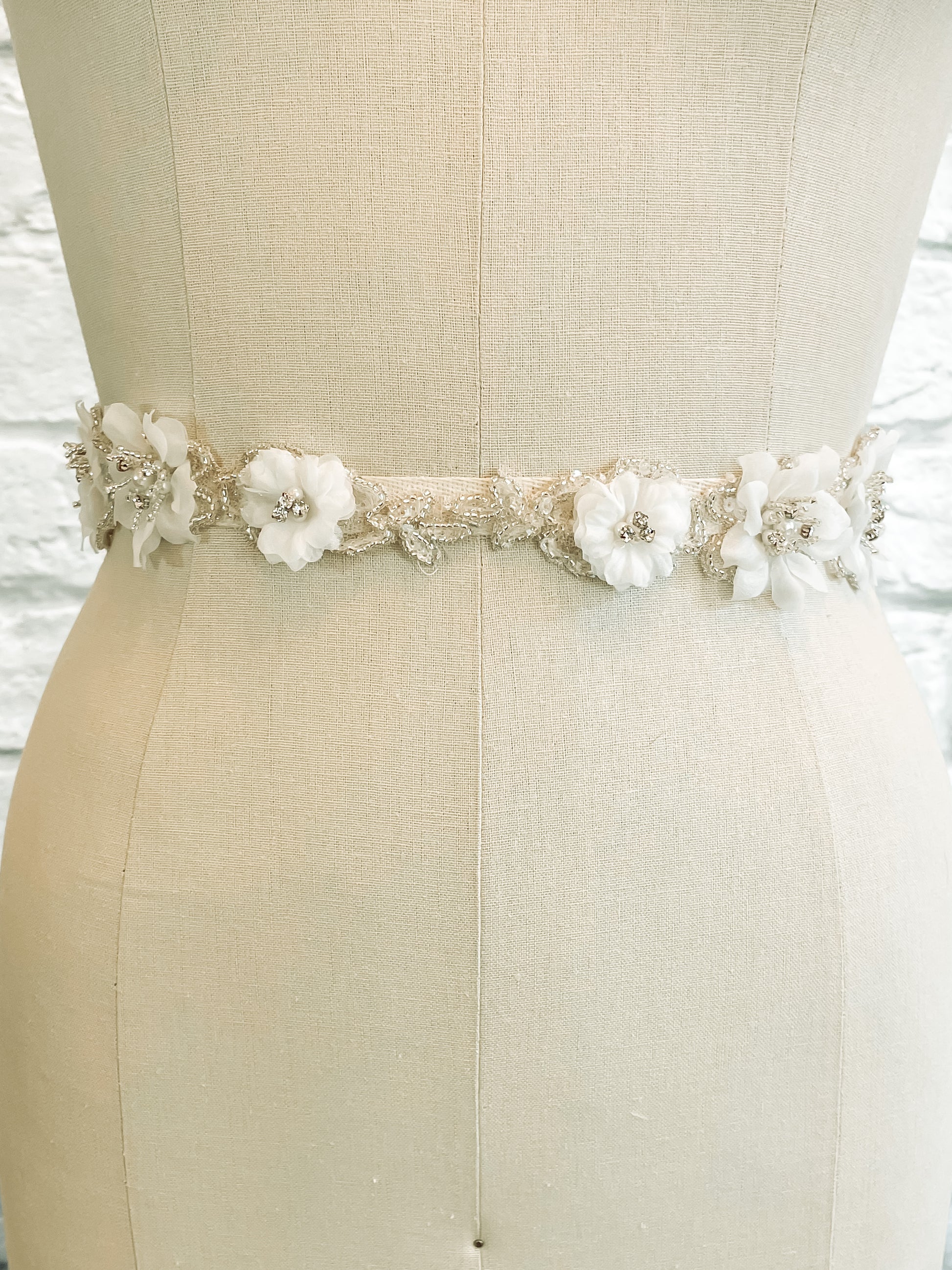 Front view of the Heidi belt on a mannequin; Close-up of the bridal belt with 3D organza flowers, pearls, and rhinestones on sheer tulle.