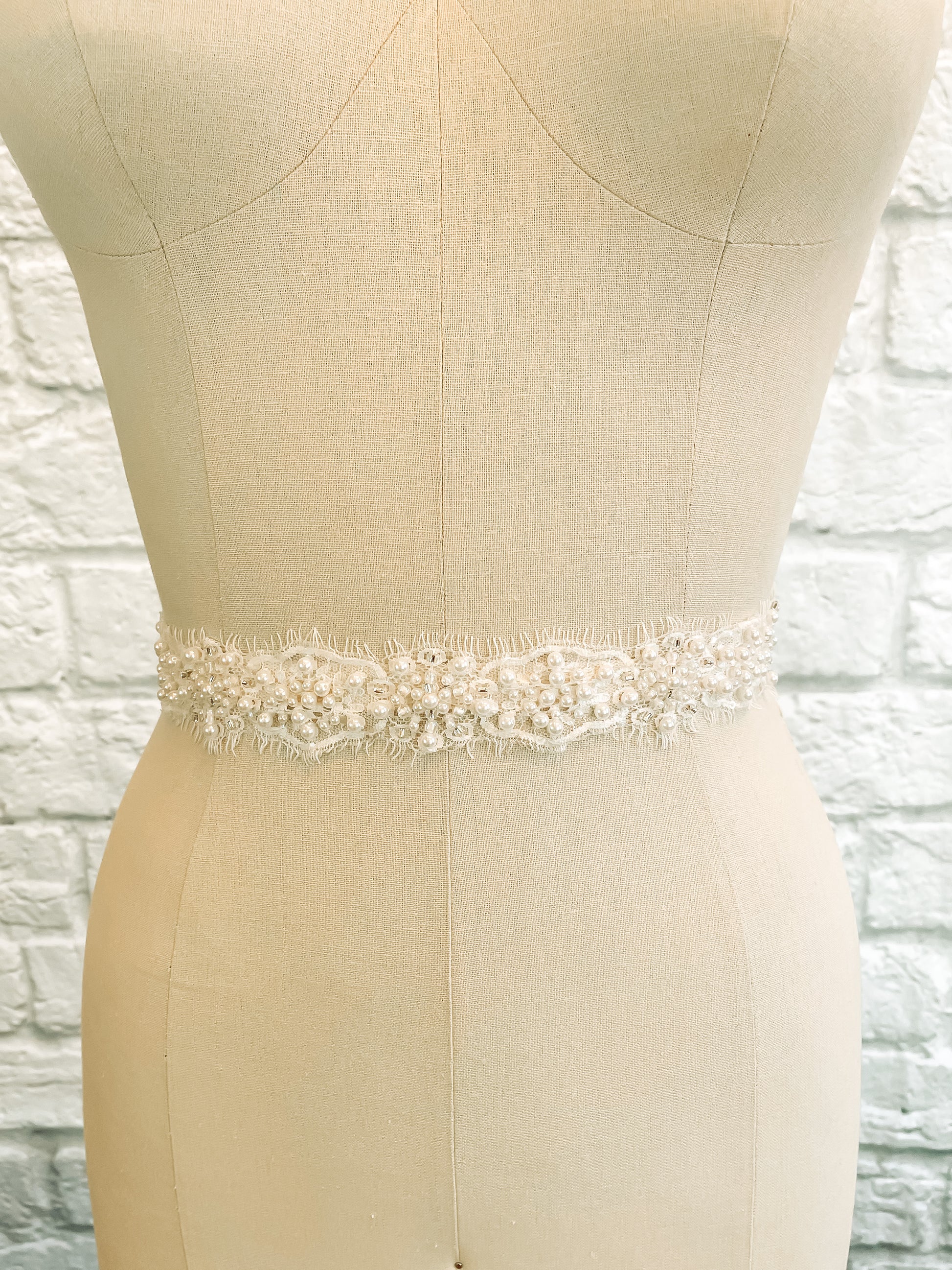 Millie bridal belt featuring pale ivory lace, clustered faux pearl beading, silver accents, and scalloped eyelash edge; romantic lace wedding sash. Displayed from the front on a mannequin