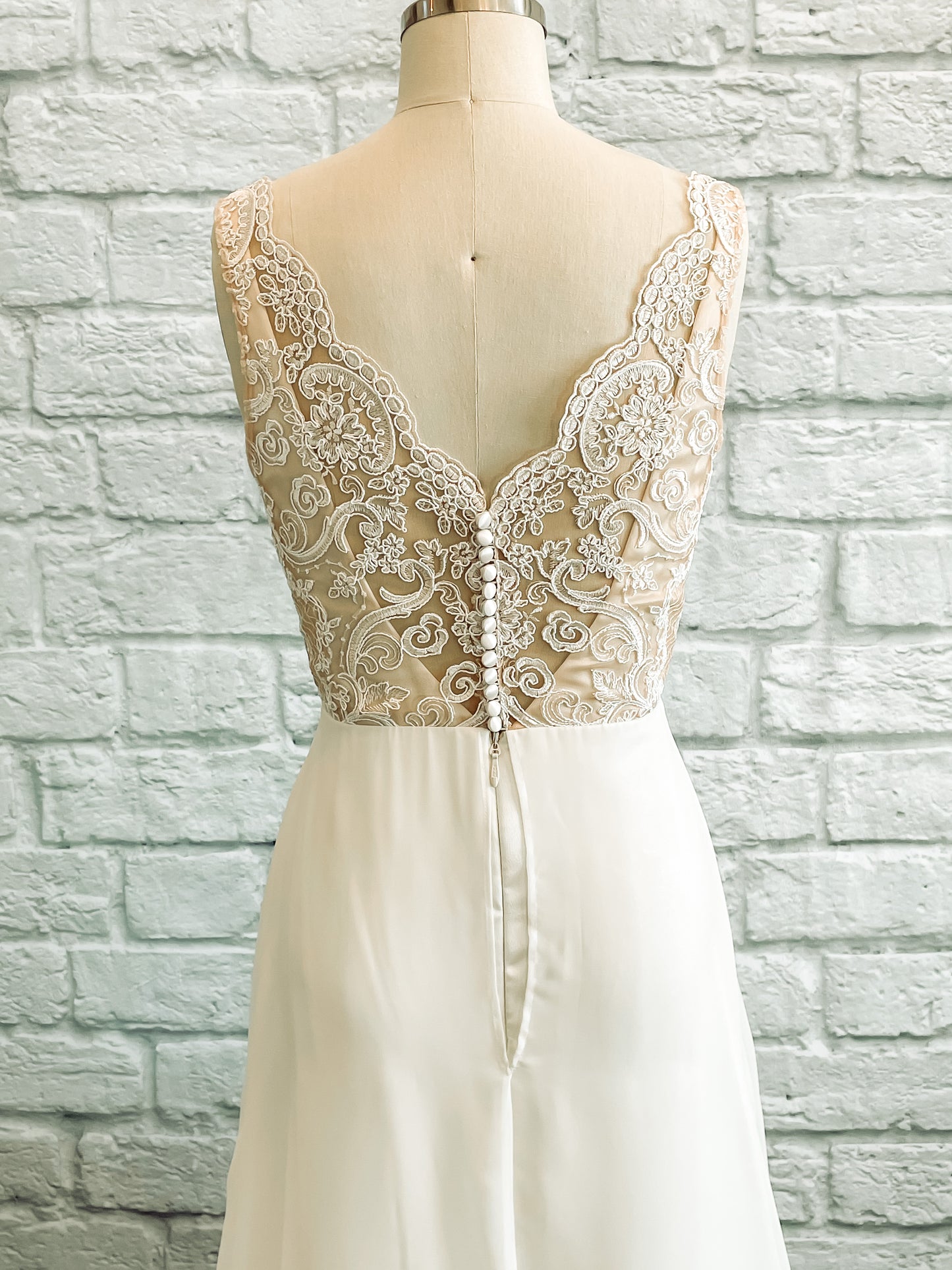 An upclose shot of the the back of Winifred on a mannequin; showing the lace pattern and scalloped v neckline with satin covered buttons.