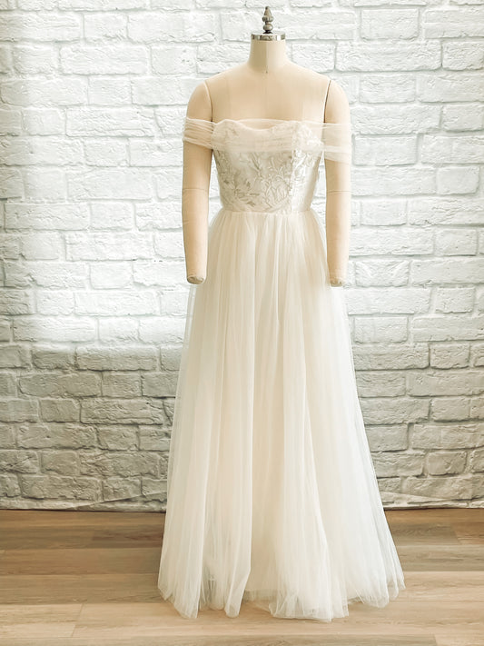 Full front view of the Penelope A-line gown with off-the-shoulder arm drape and gathered glitter tullé skirt with a strapless sweetheart neckline.