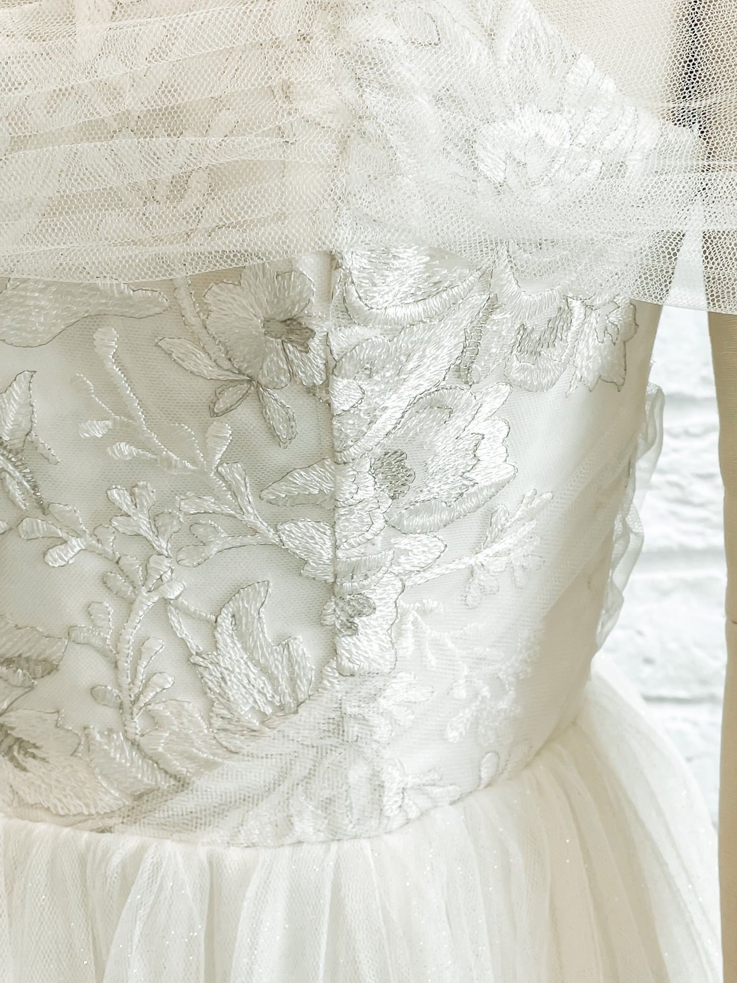 Close-up of silver threadwork in the bodice lace of the Penelope gown with the off the shoulder tulle drape and gathered tulle detailing at the waist.