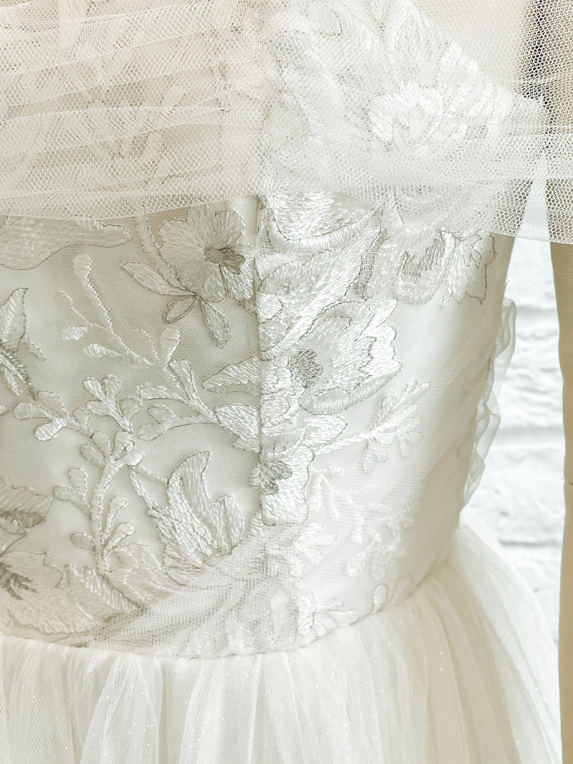 Close-up of silver threadwork in the bodice lace of the Penelope gown with the off the shoulder tulle drape and gathered tulle detailing at the waist.