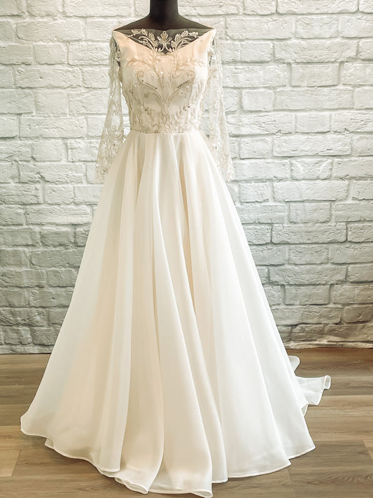 A full front view of the Theodora gown on a mennequin; the Theodora wedding gown is showing the modest boat neckline and ¾ lace sleeves with an extra full circle skirt.