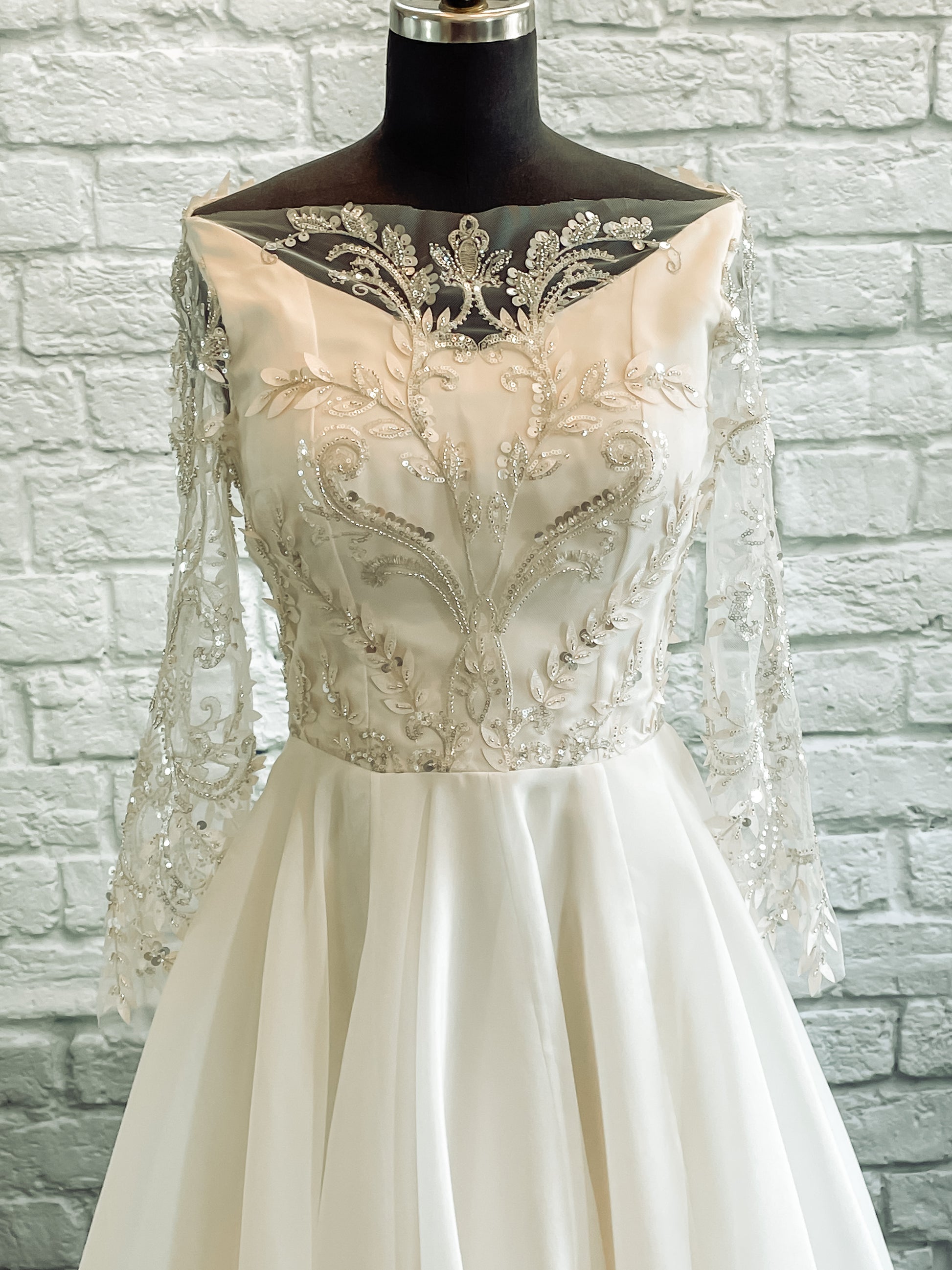 A close up of the Theodora wedding dresses bodice and waist seam; the lace detail and pattern in the focus with the Silver embroidery, swoops, and beaded details that reflect across the bodice symmetrically.