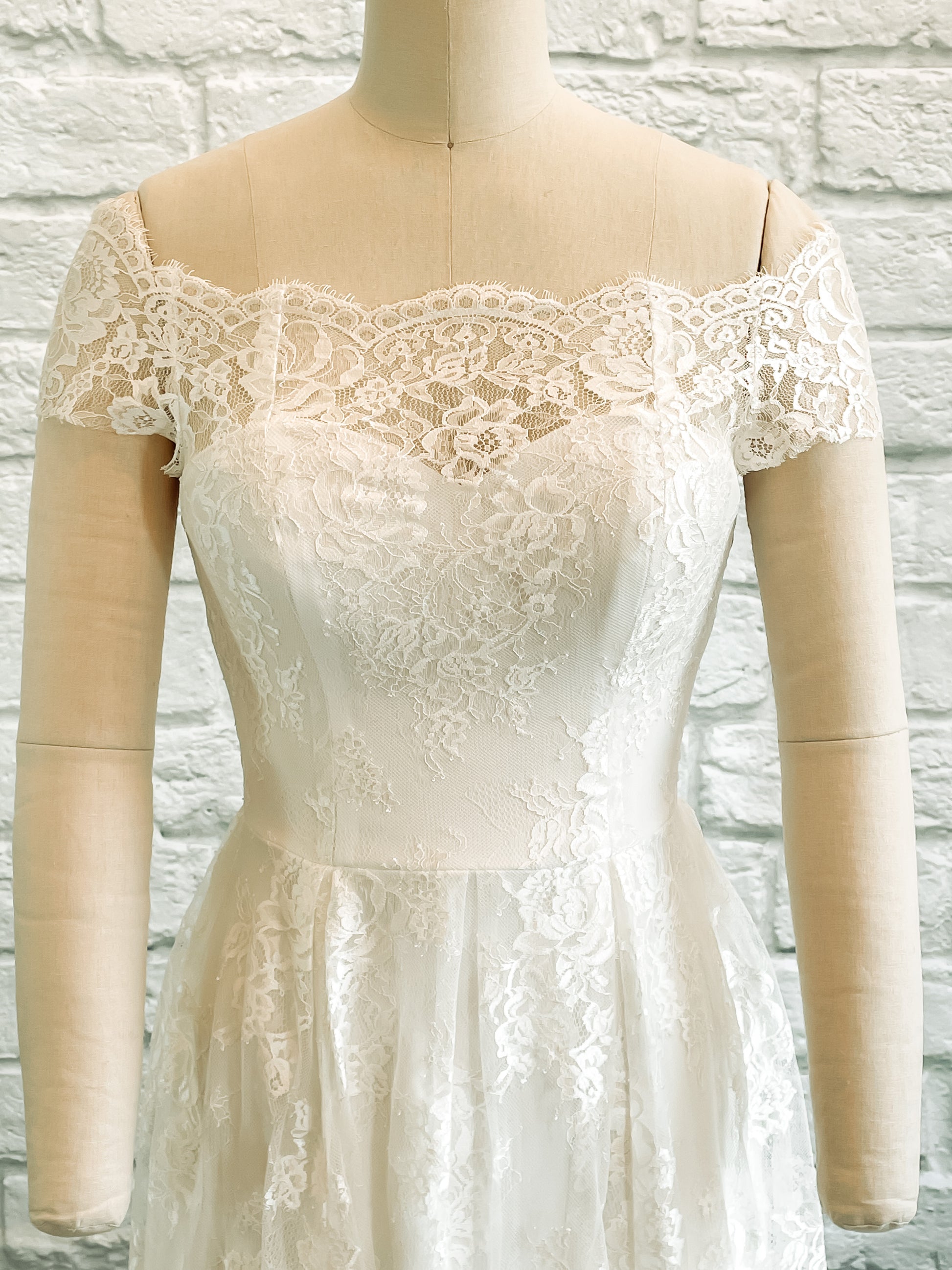 A close up of the Serafina wedding gowns bodice and the top of the skirt; it is showing the sweetheart crepe neckline and off-the-shoulder lace sleeves.