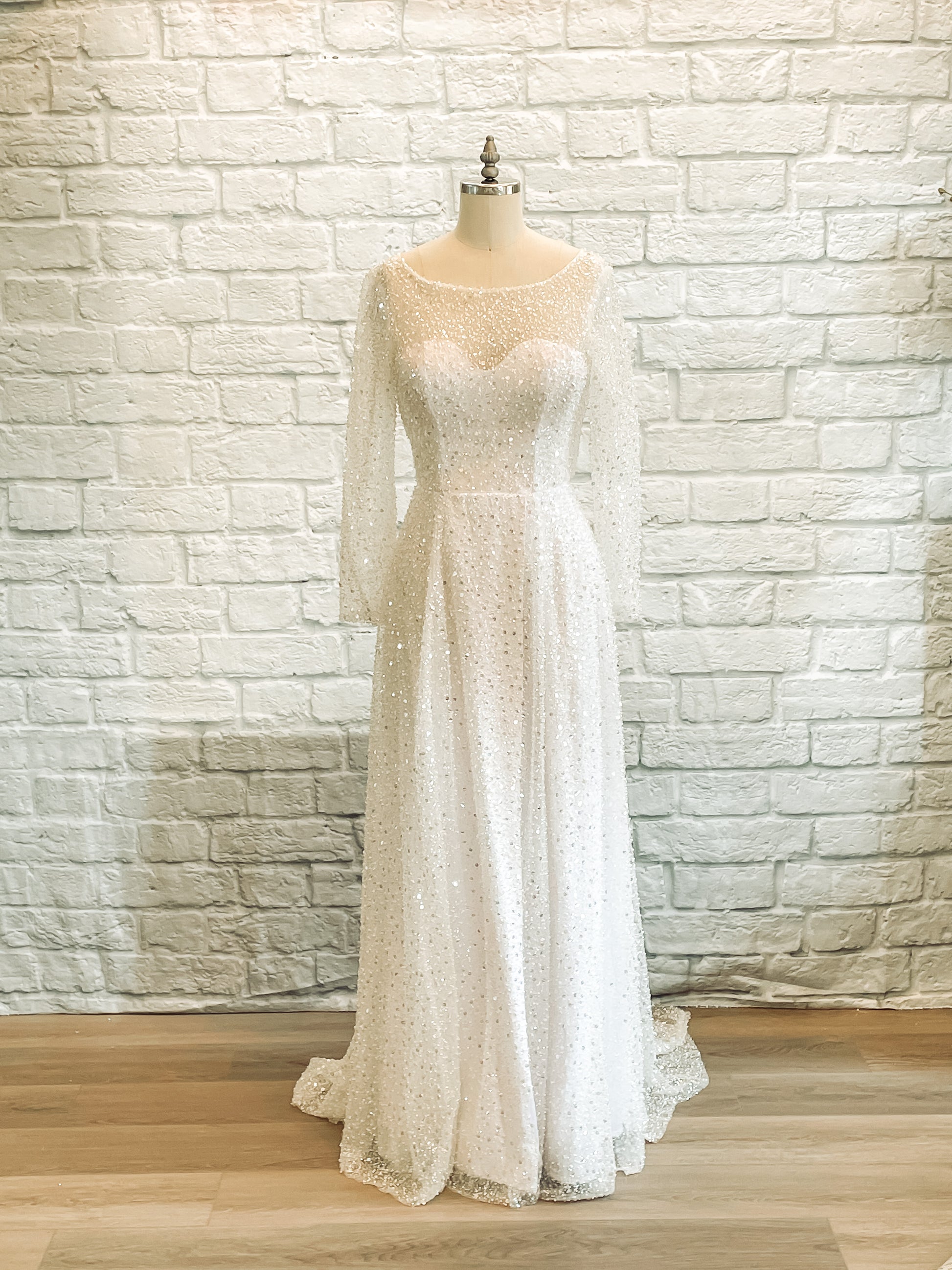 Full-length image of Faelynn wedding gown on mannequin, showing sheer overlay, boat neckline, and mock wrap skirt.