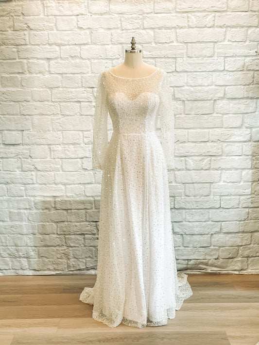 Full-length image of Faelynn wedding gown on mannequin, showing sheer overlay, boat neckline, and mock wrap skirt.