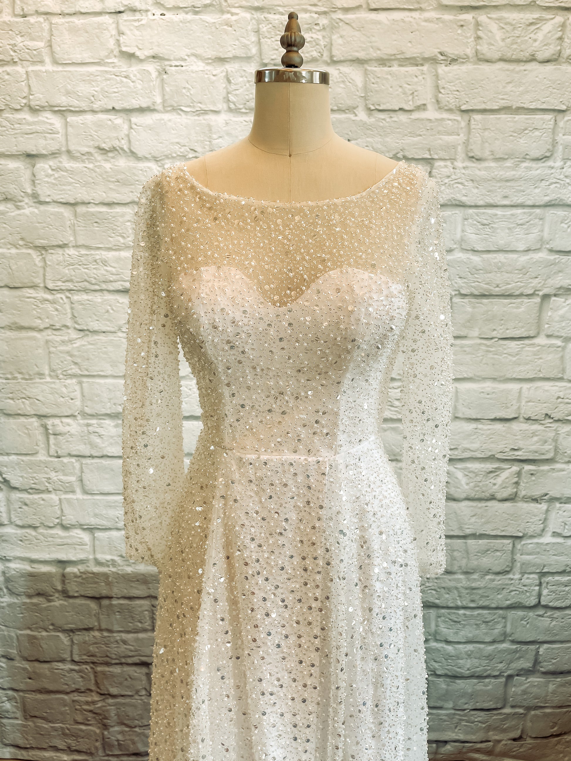Detail of sweetheart satin bodice under beaded tulle overlay with long beaded sleeves.