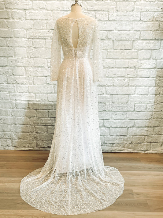 Rear view of Faelynn gown showing high bateau back, sheer sleeves, and flowing train.