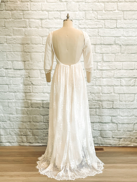 Back view of the Avabelle gown on a mannequin, showing the dramatic low scoop back and delicate scalloped lace train extending behind the mannequin.