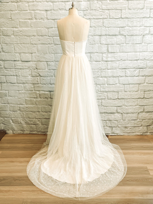 Back view of the Beatrice wedding dress, highlighting the layered tulle and lace train that extends gracefully behind in soft, airy tiers.