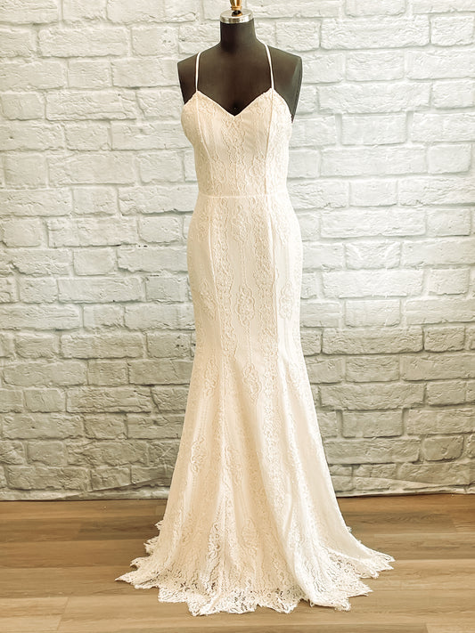 A full front shot of the Willoughby gown on a mannequin; the gown features a V neckline, a softly draped lower skirt and vertical lace lines.