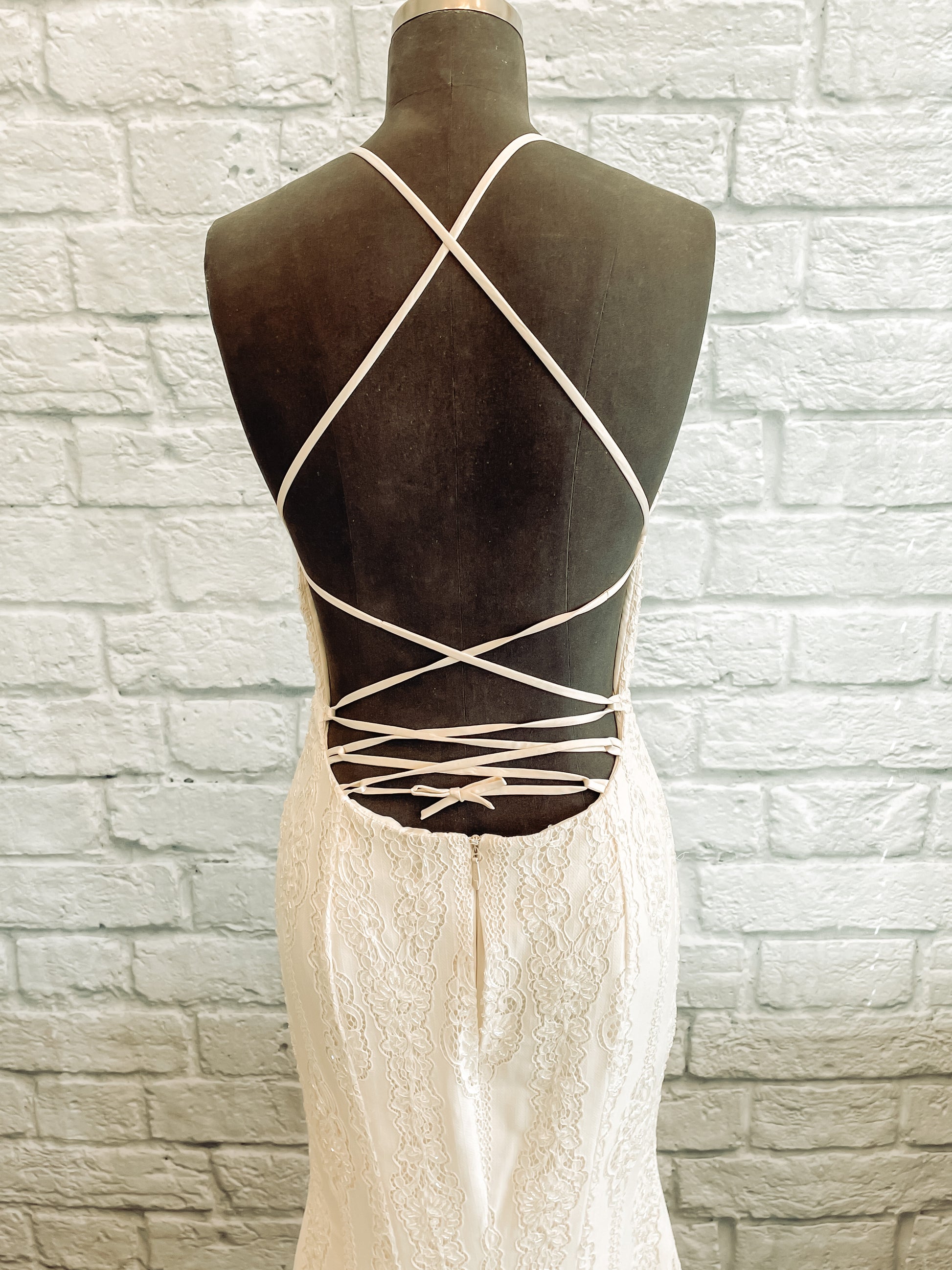 A close up image of the back of the Willoughby gown on a mannequin; showing off the crisscross strap detailing, and fitted shape through the hips.