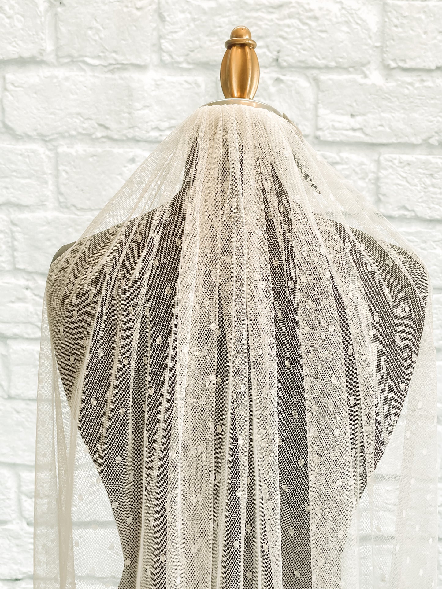 A close up of the gathered comb and top pf the swiss dot veil, scarlett. displayed on a dark mannequin you an easily see the ¼" dots on tulle veil.