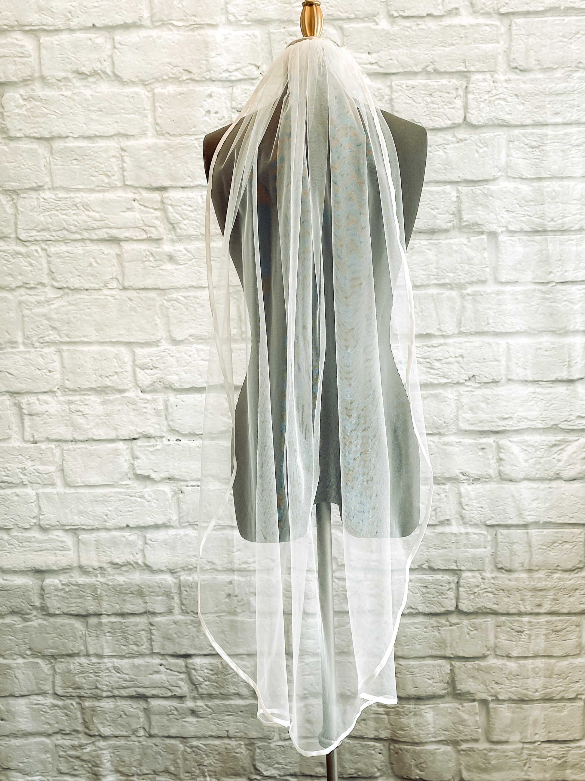 A closer image of the bridget veil hung up on a mannequin in white calf length.