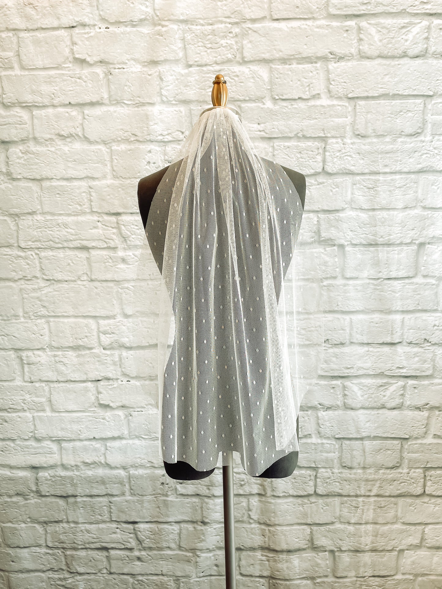 Another Scarlett dot veil made from a swiss dot tulle and comb; it is being shown against a dark grey mannequin and is shown in this image in a Fingertip length.