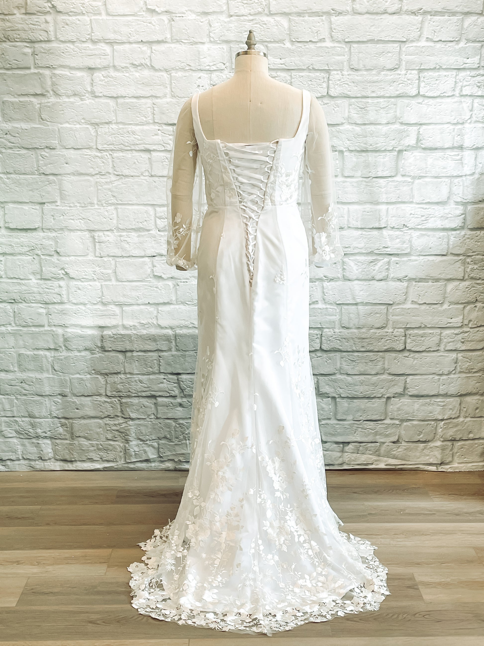 Full length back shot of the Violet gown on a mannequin; featuring the Lace-up corset and floral lace train.