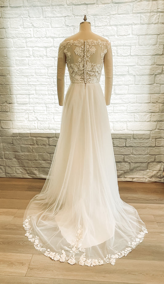 Full-length back view of the dress on a mannequin, highlighting the illusion back with satin buttons and dual train lengths in satin and tulle