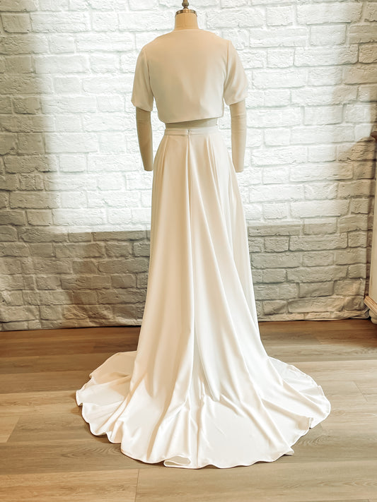 Back view of the Cassie two-piece bridal set on a mannequin, showing the high back neckline of the top, short sleeves, and medium train of the A-line skirt.