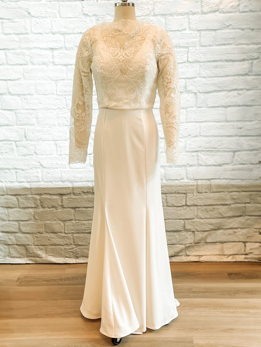 A full front image of the Zuri gown on a mannequin; the gown is a mock neck lace wedding gown with mermaid silhouette and long lace sleeves.