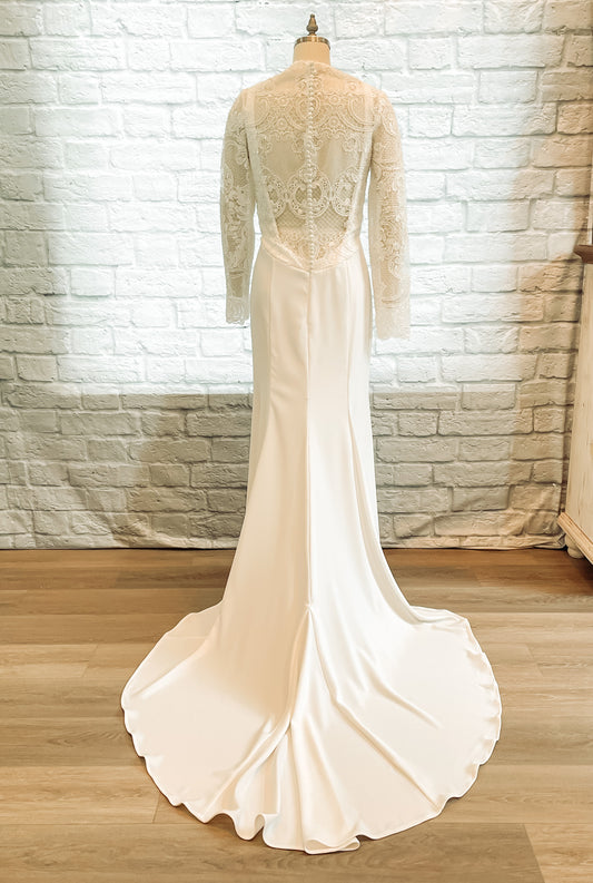 A full back image of the Zuri wedding gown on a mannequin; the Lace overlay with bridal buttons and low crepe back neckline bring the eye down to the elongated train.