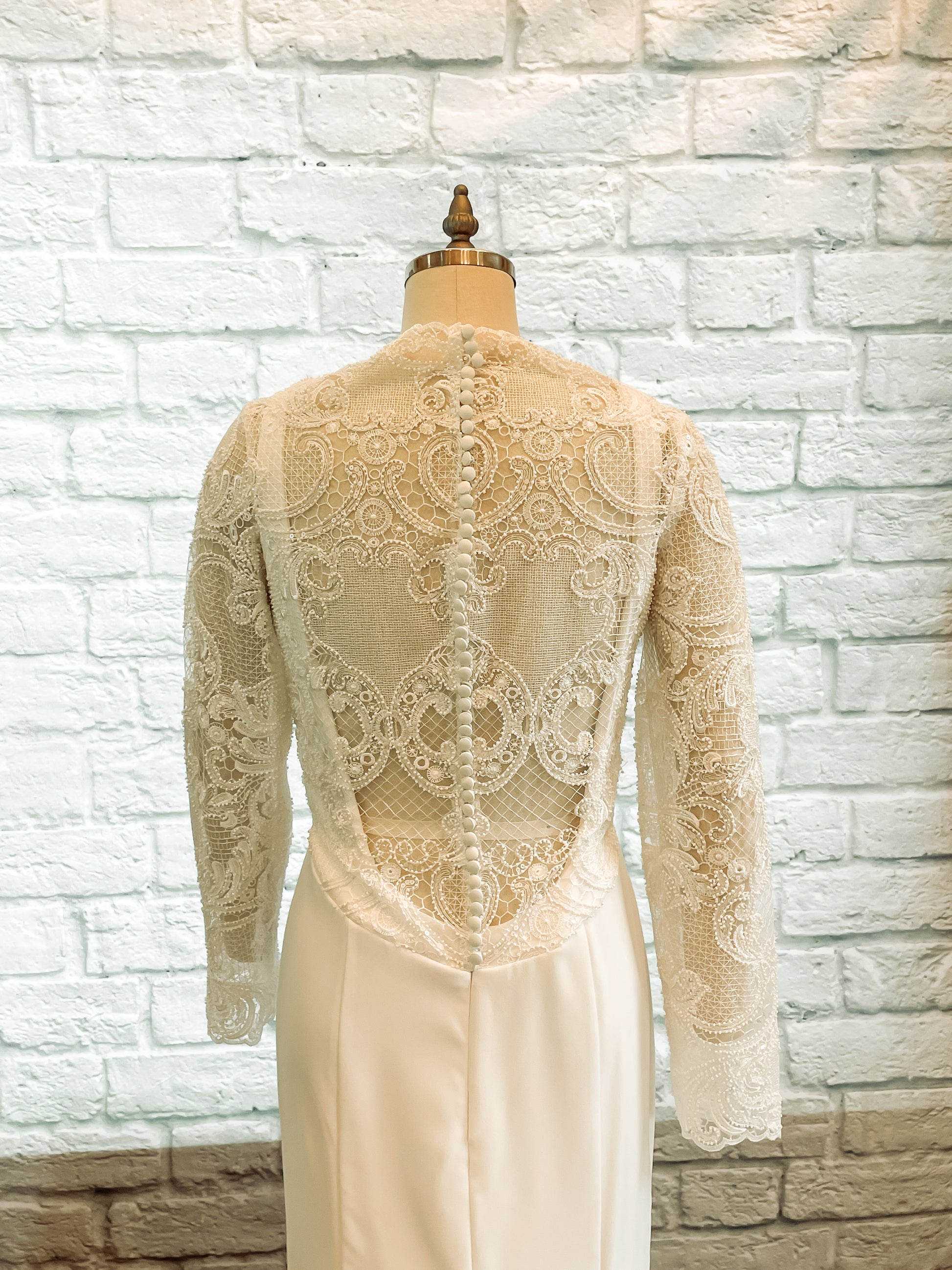 A close up of the back bodice of the Zuri gown with geometric lace, satin covered bridal buttons and fitted crepe base.