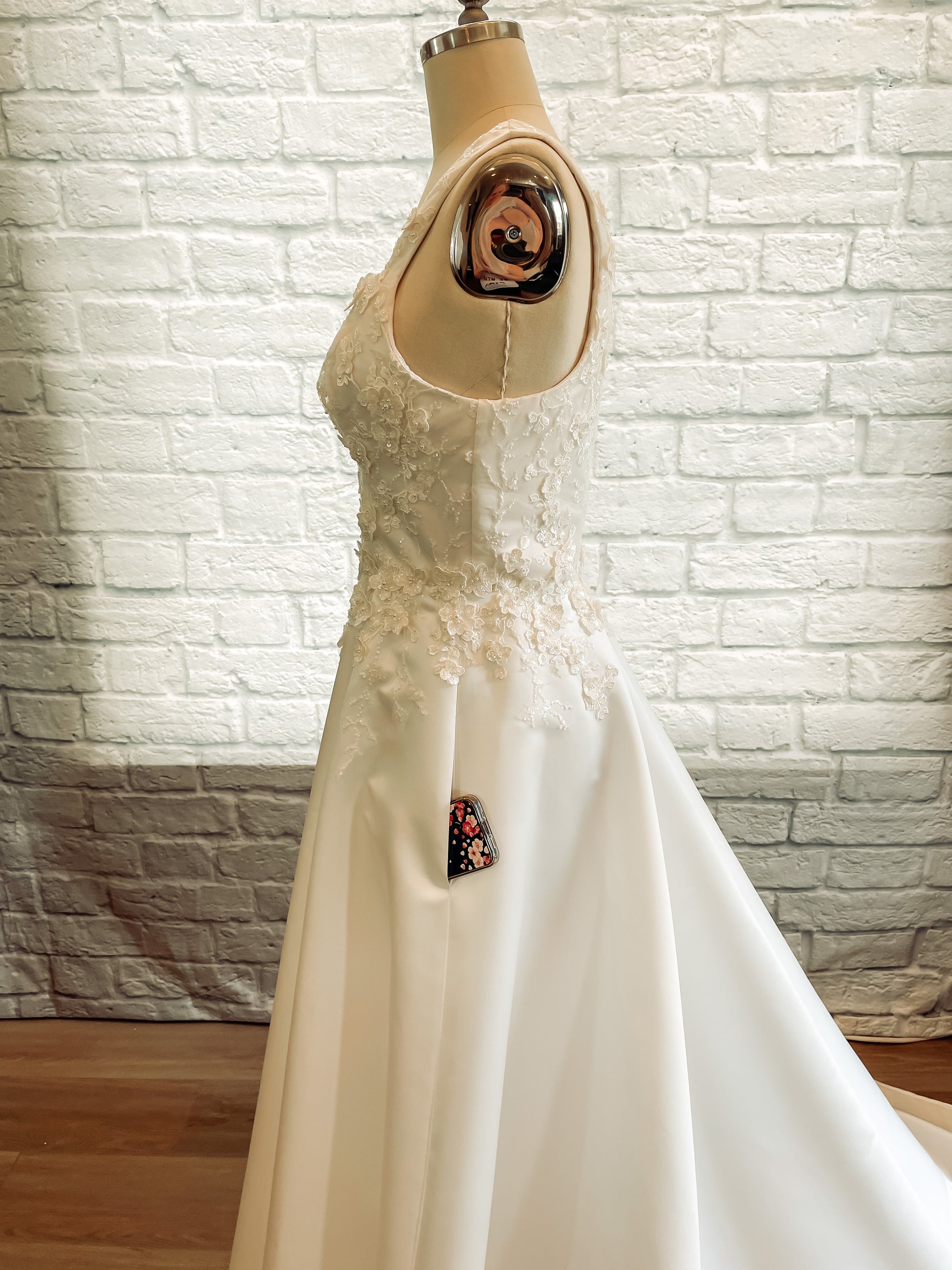A side view of the Sabina wedding gown on a mannequin,  a phone is poking out of the hidden pocket in the side seams.