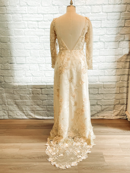 A full length back view of the Reagan wedding dress with an Open back, dramatic V-shaped lace neckline, and an eighteen inch long train.