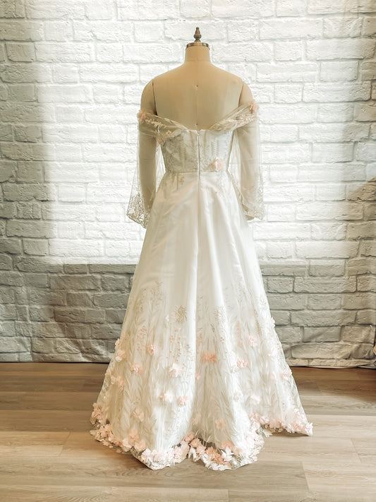 Full back view of the Prue gown on a mannequin it has an A-line skirt with lace extending from hem, off the shoulder straps and bishop sleeves.