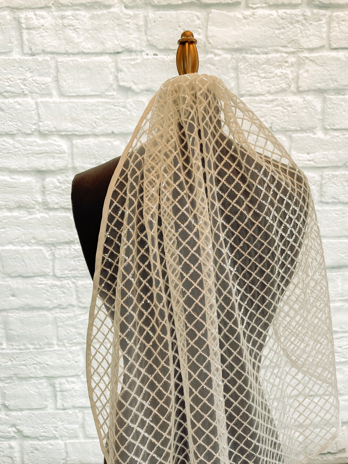A close up photo of the Gloria wedding veil with sequined diamond pattern and ribbon edge.