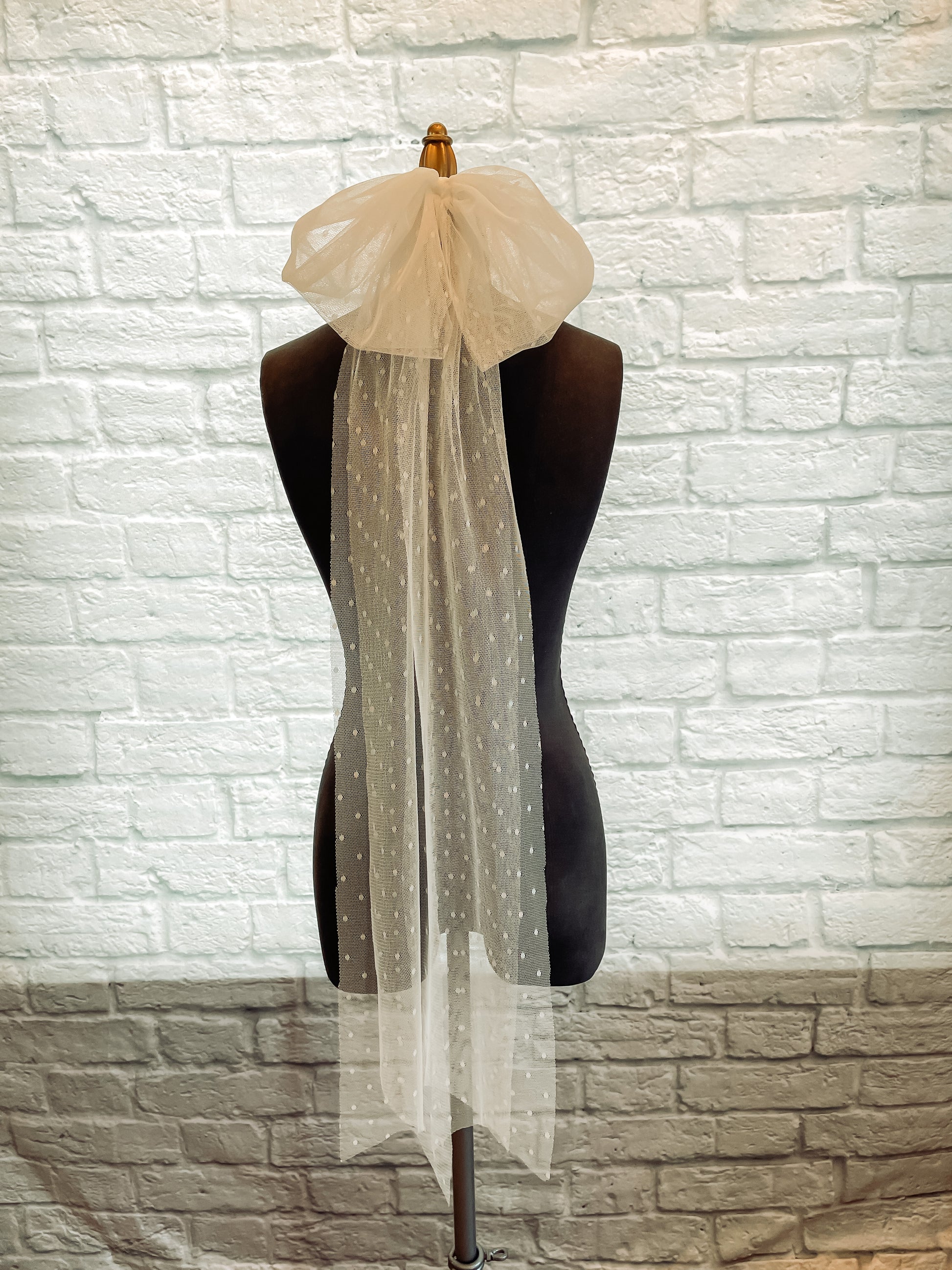 A bridal bow veil displayed on a mannequin in swiss dot fabric in a fingertip length.