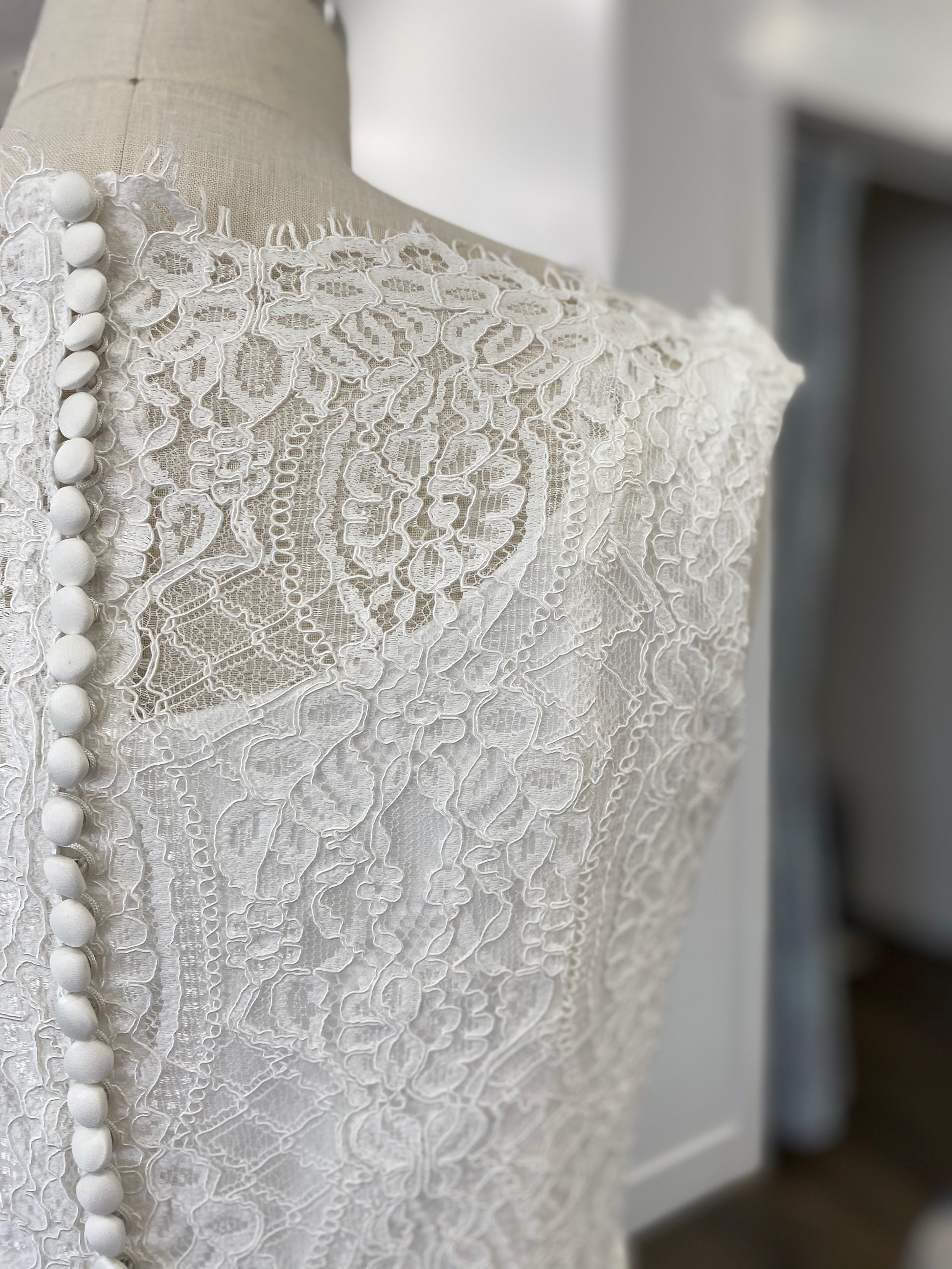 Detail of the floral lace overlay on the Blair gown, showing the mix of vertical trellis lines, floral patterns, and diamond lacework.
