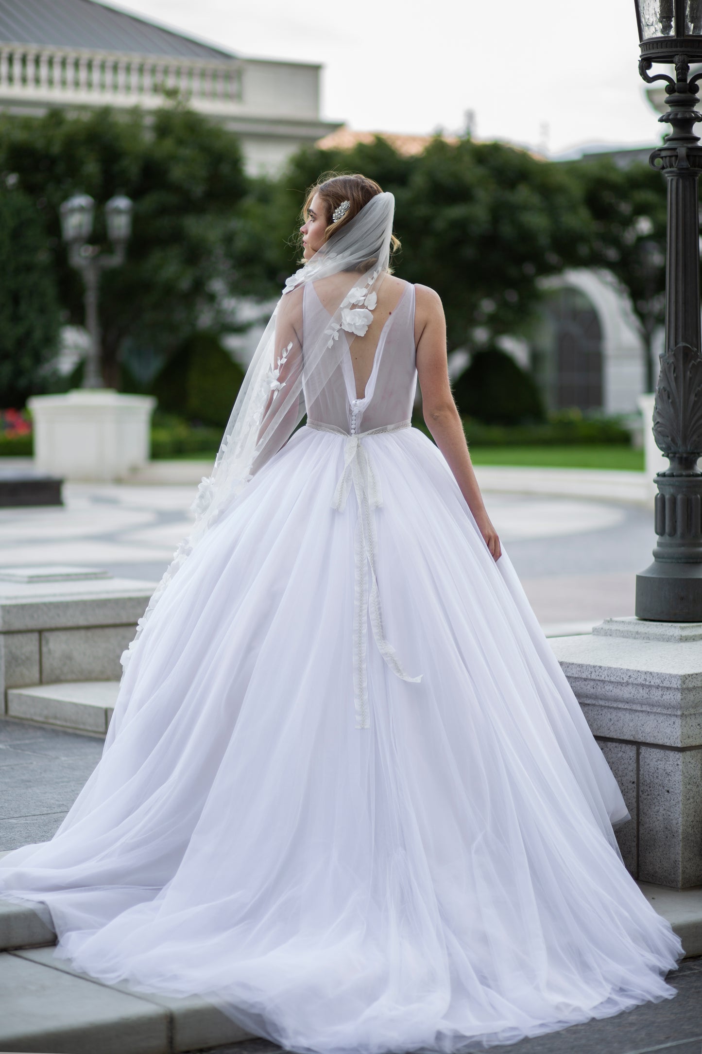 A photo of a bride wearing the persephone gown, fleur belt and Celine veil. The veil has been swept to the side so it lays on the side of the ballgown.