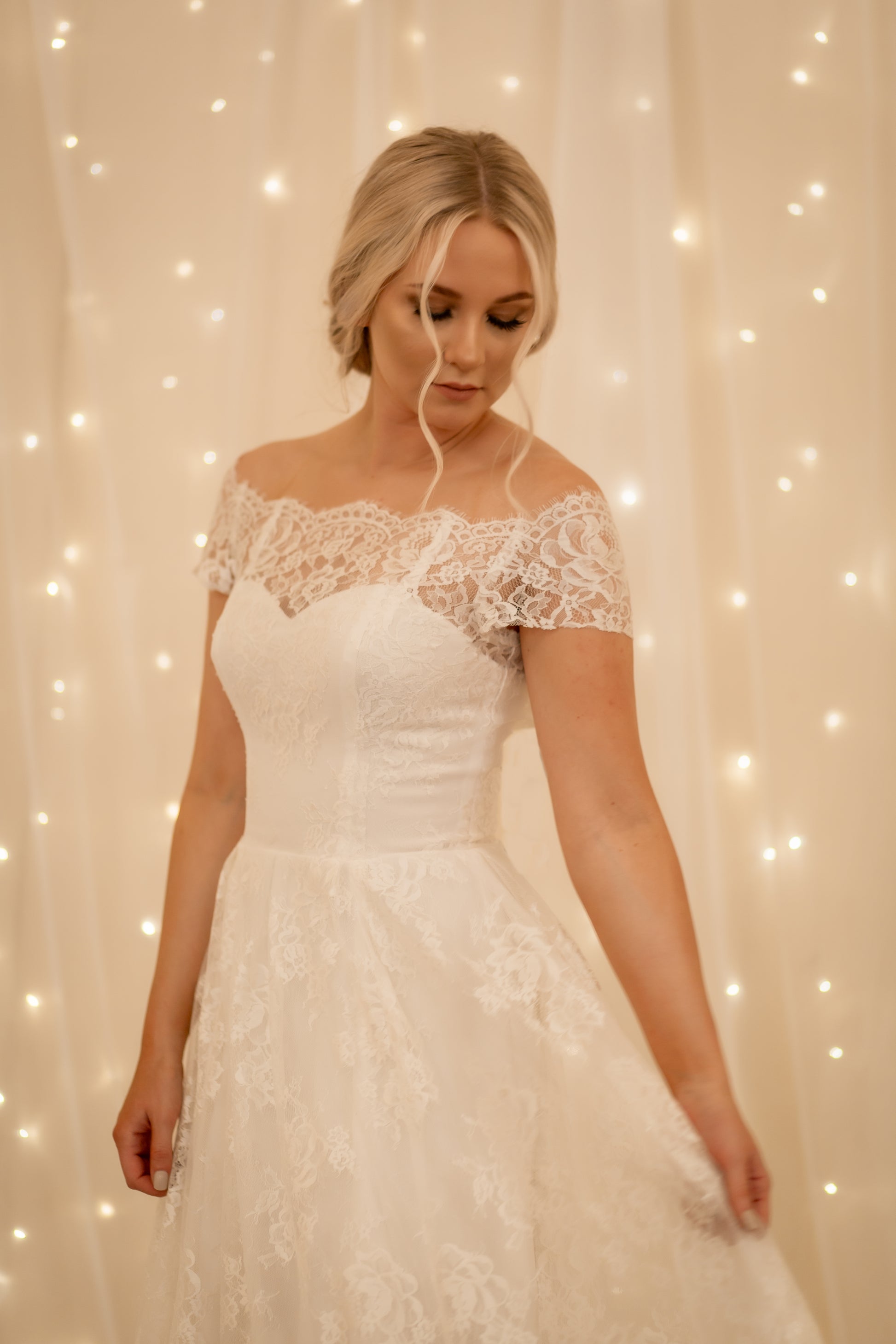 A close up image of a bride wearing the Serafina gown, her structured bodice fits her perfectly as she holds the lace out to the side gently.