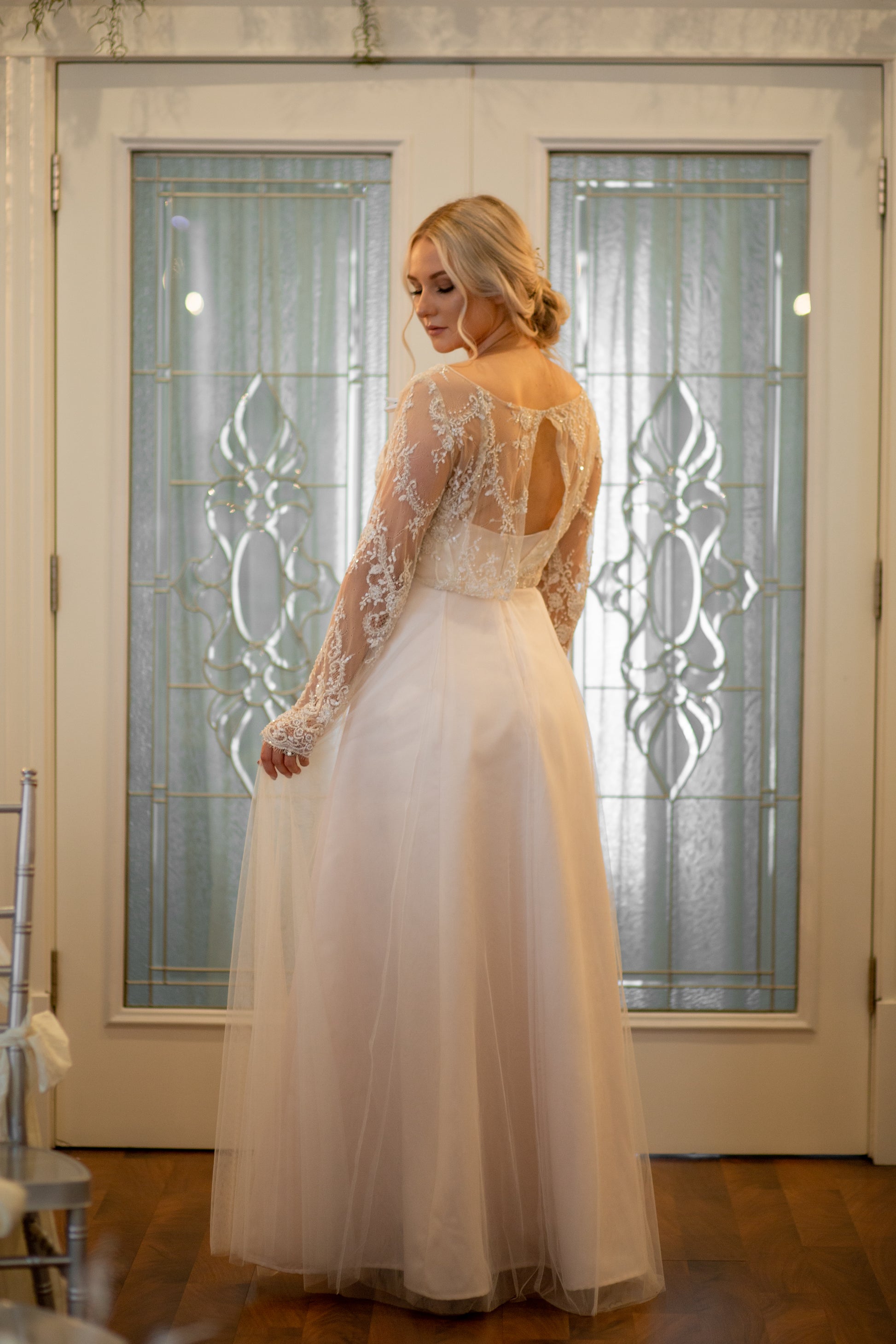 A ¾ back view of the bride wearing Eivissa gown, showcasing fitted lace sleeve, keyhole back, and gentle A-line silhouette.