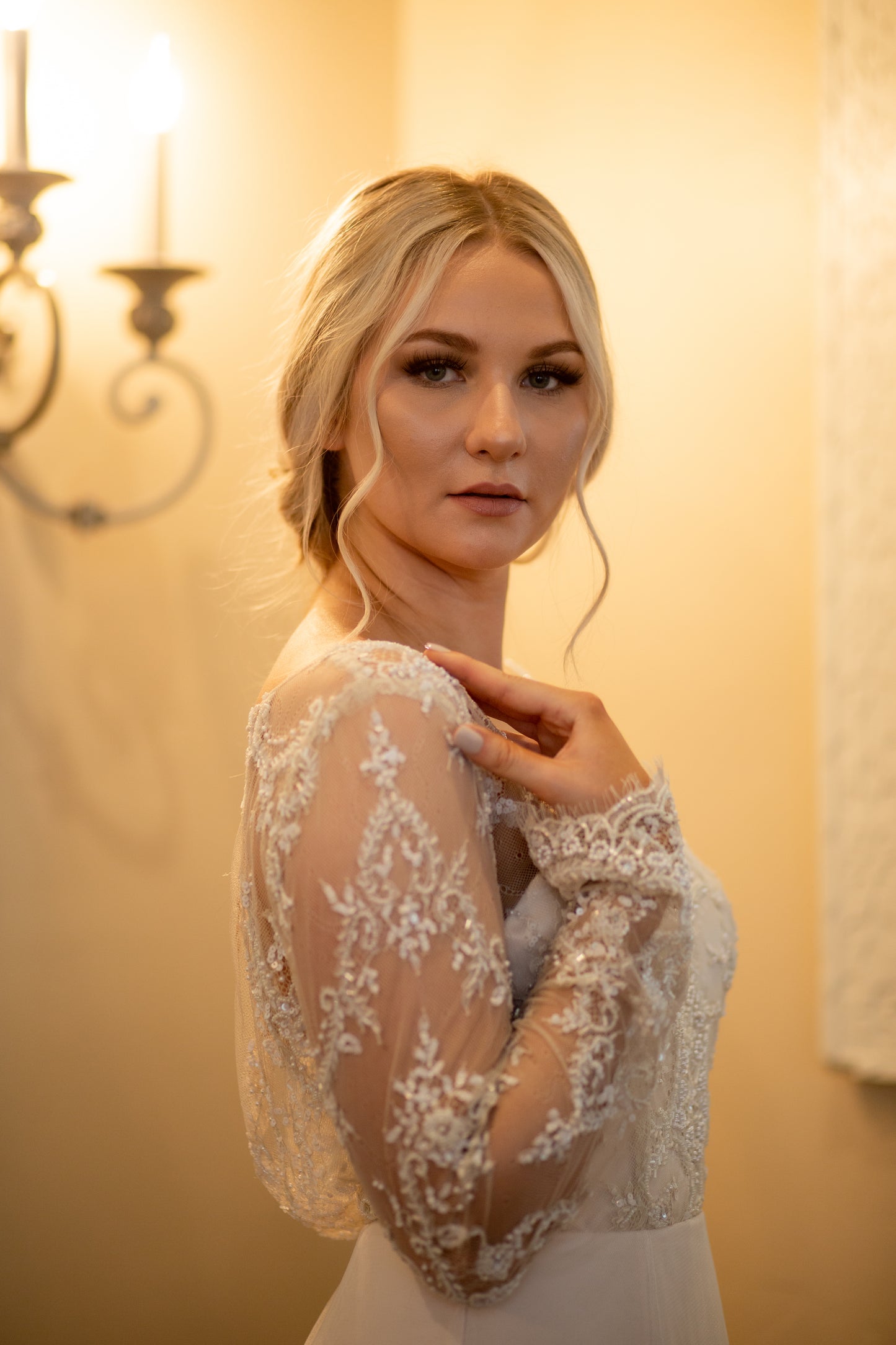 Side profile of bride in Eivissa gown, with her hand placed on her shoulder you can see the sheer lace sleeve and the rise and fall of the beaded pattern.